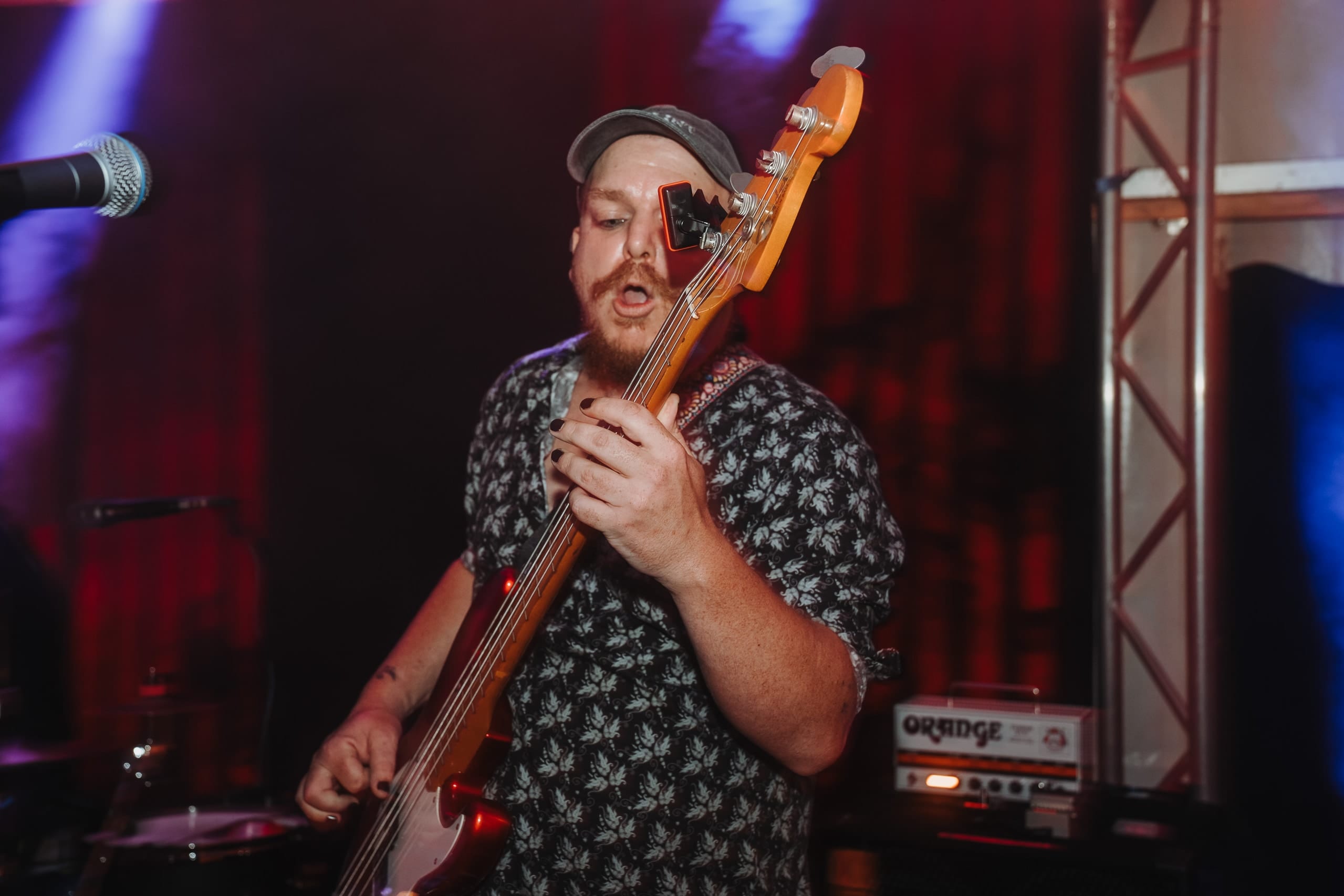 Ein Bassist mit Mütze reckt den Bass in die Höhe, im roten Licht