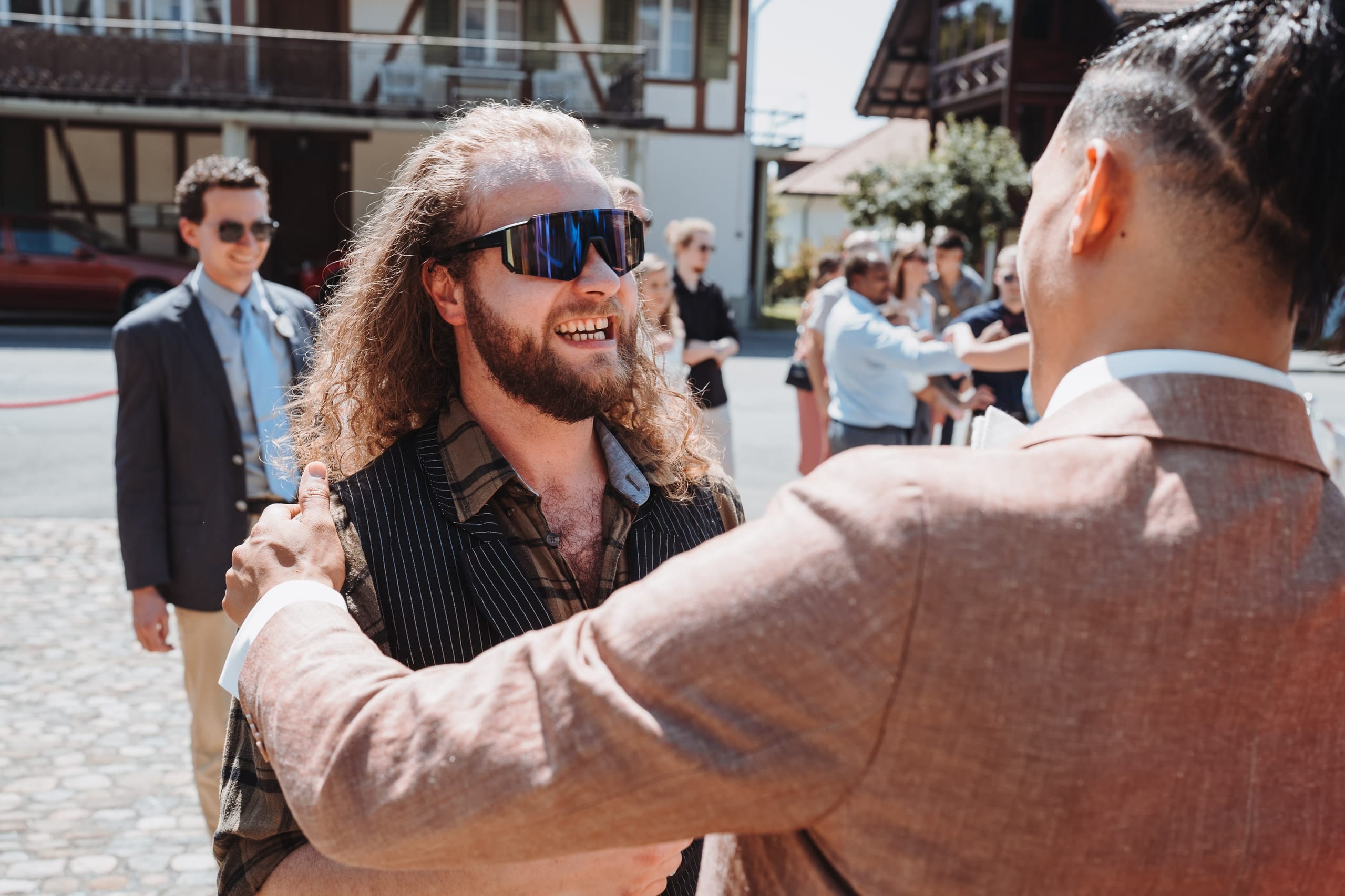 Der Bräutigam umarmt einen Gast mit Sonnenbrille und langen Haaren