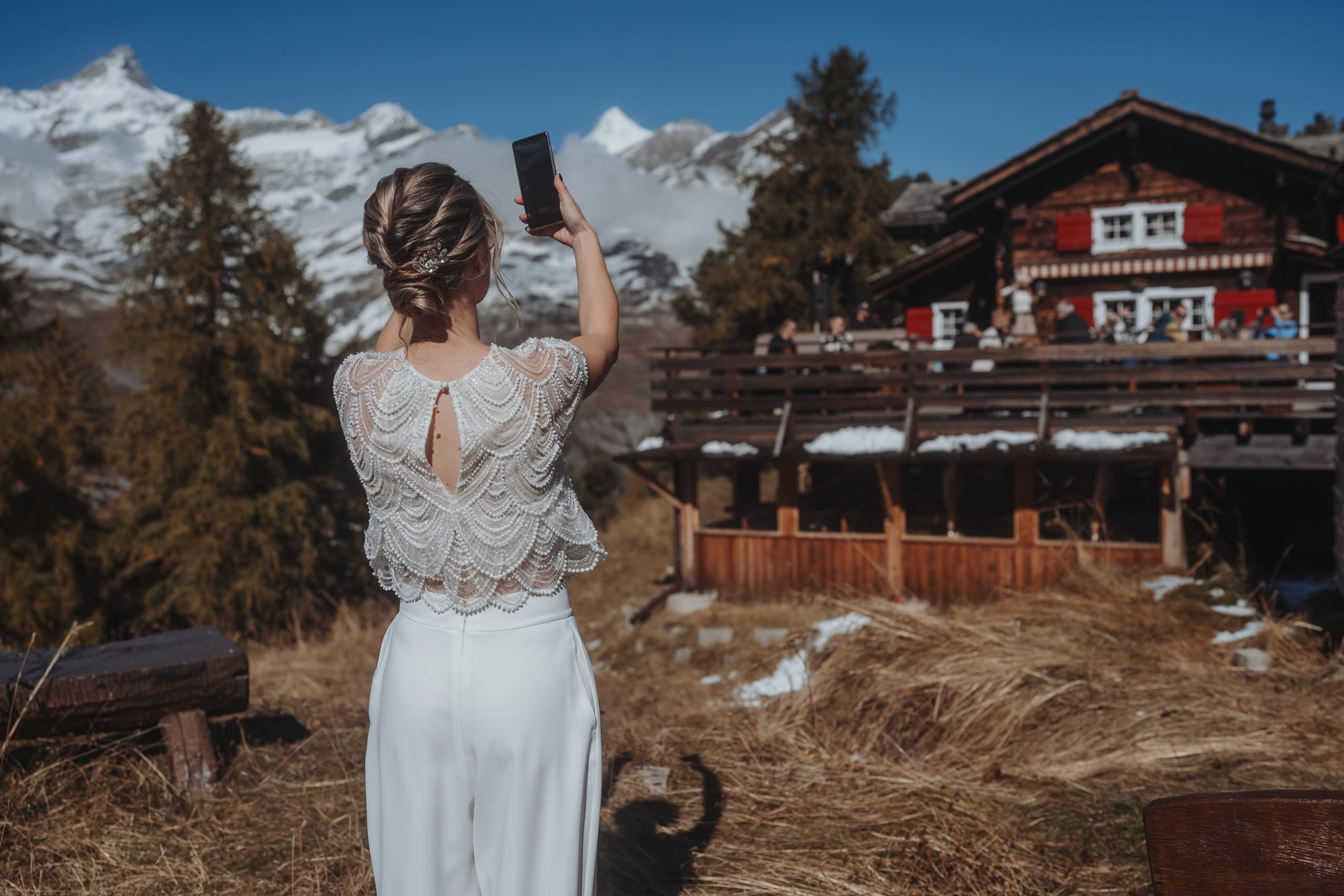 Die Braut fotografiert mit dem Handy ein Bergrestaurant aus Holz mit roten Fensterläden