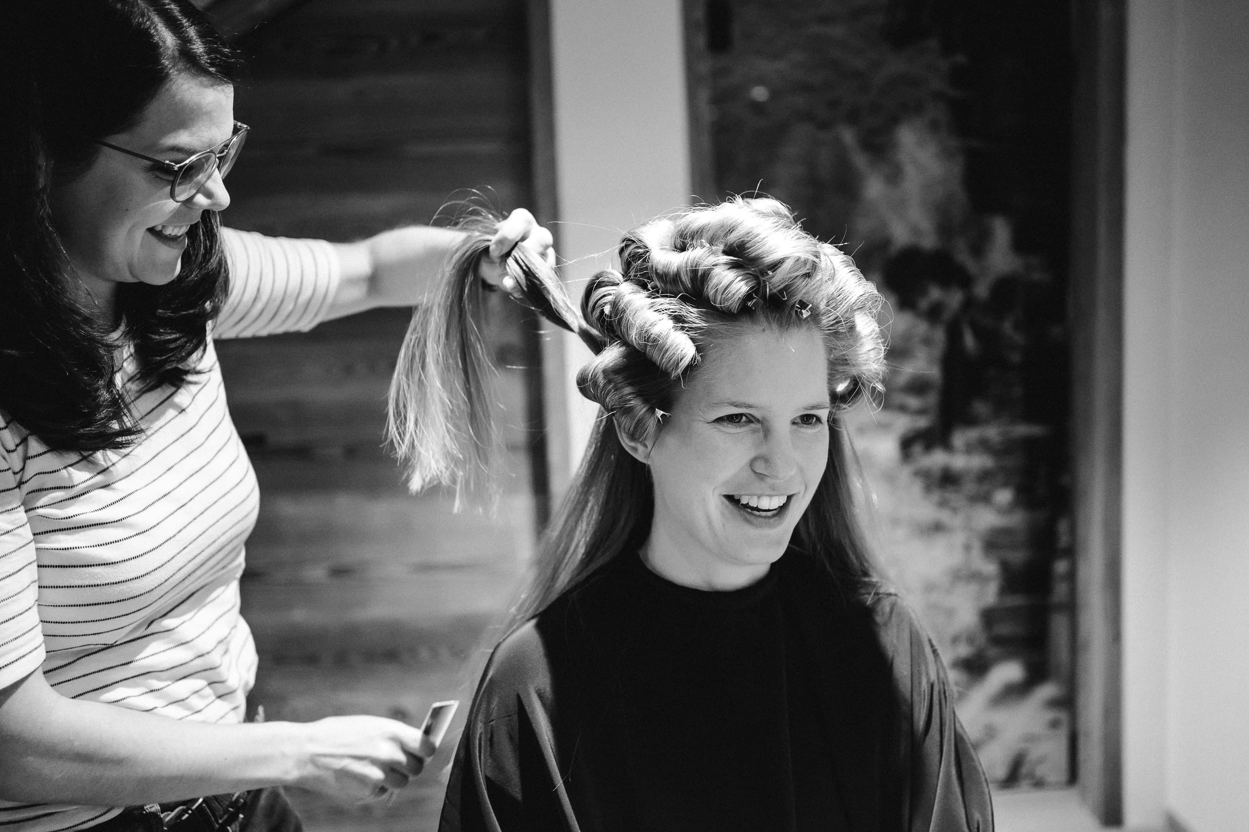 Schwarzweiss: Die Braut lacht, während ihre Haare eingedreht werden
