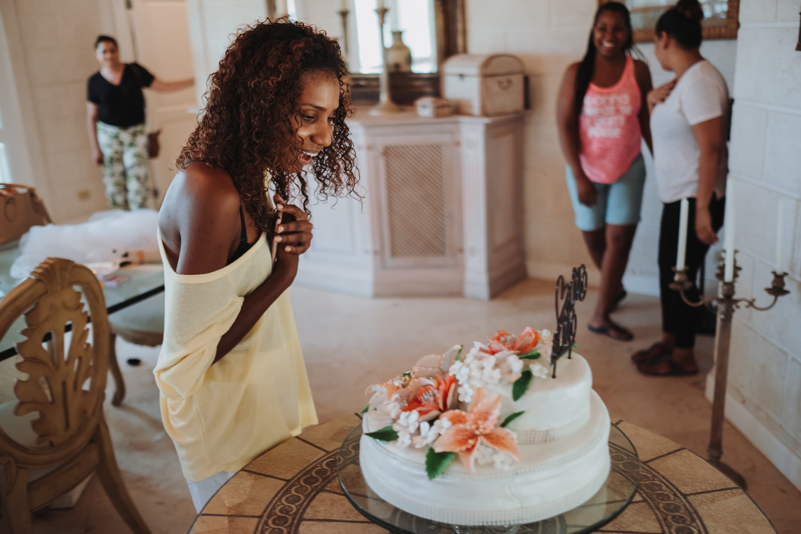 Die Braut betrachtet lächelnd die Hochzeitstorte mit orangen Lilien, hinter ihr drei Frauen
