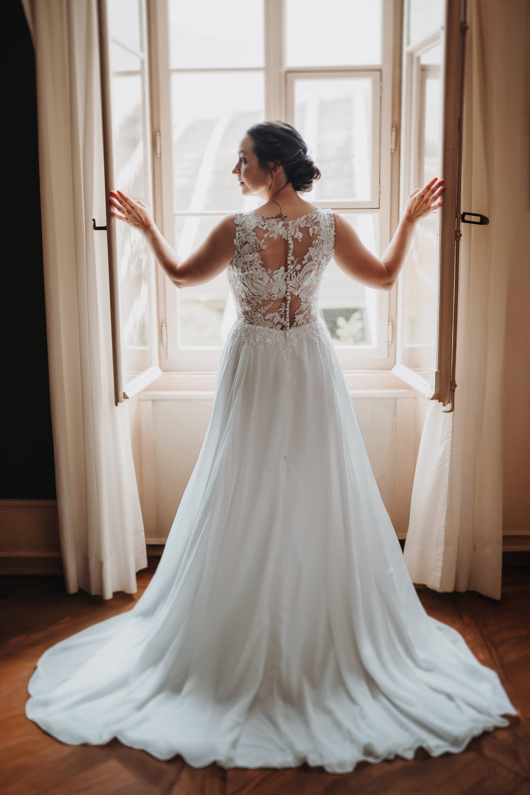 Die Braut im Kleid am offenen Fenster, von hinten