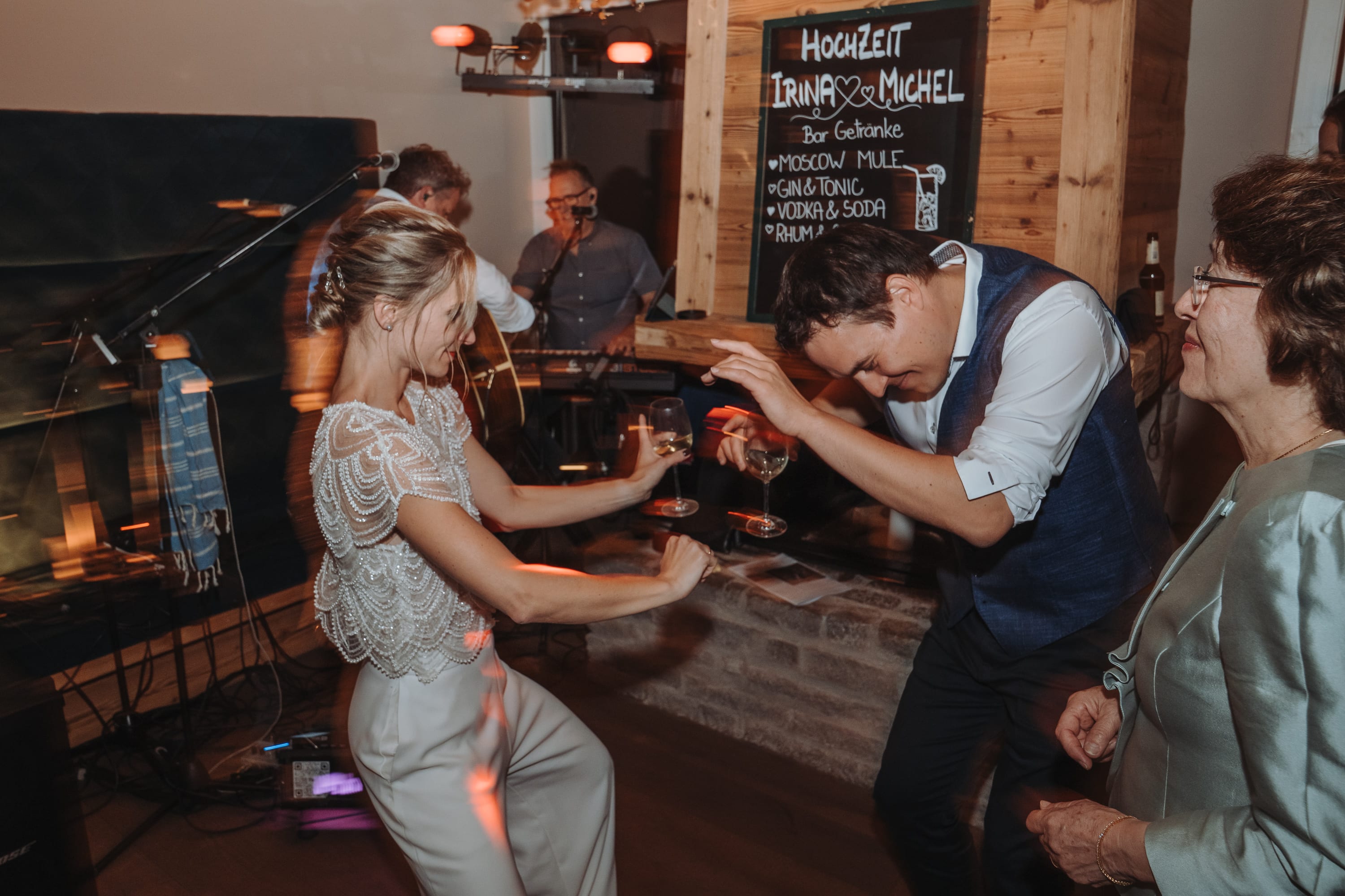 Die Braut tanzt ausgelassen mit einem Gast vor der Bar