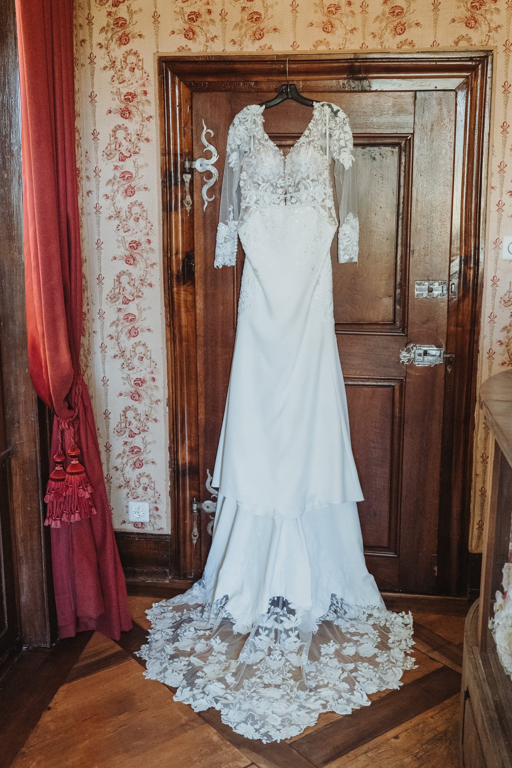 Das Brautkleid hängt an einer alten Holztür vor geblümter Tapete