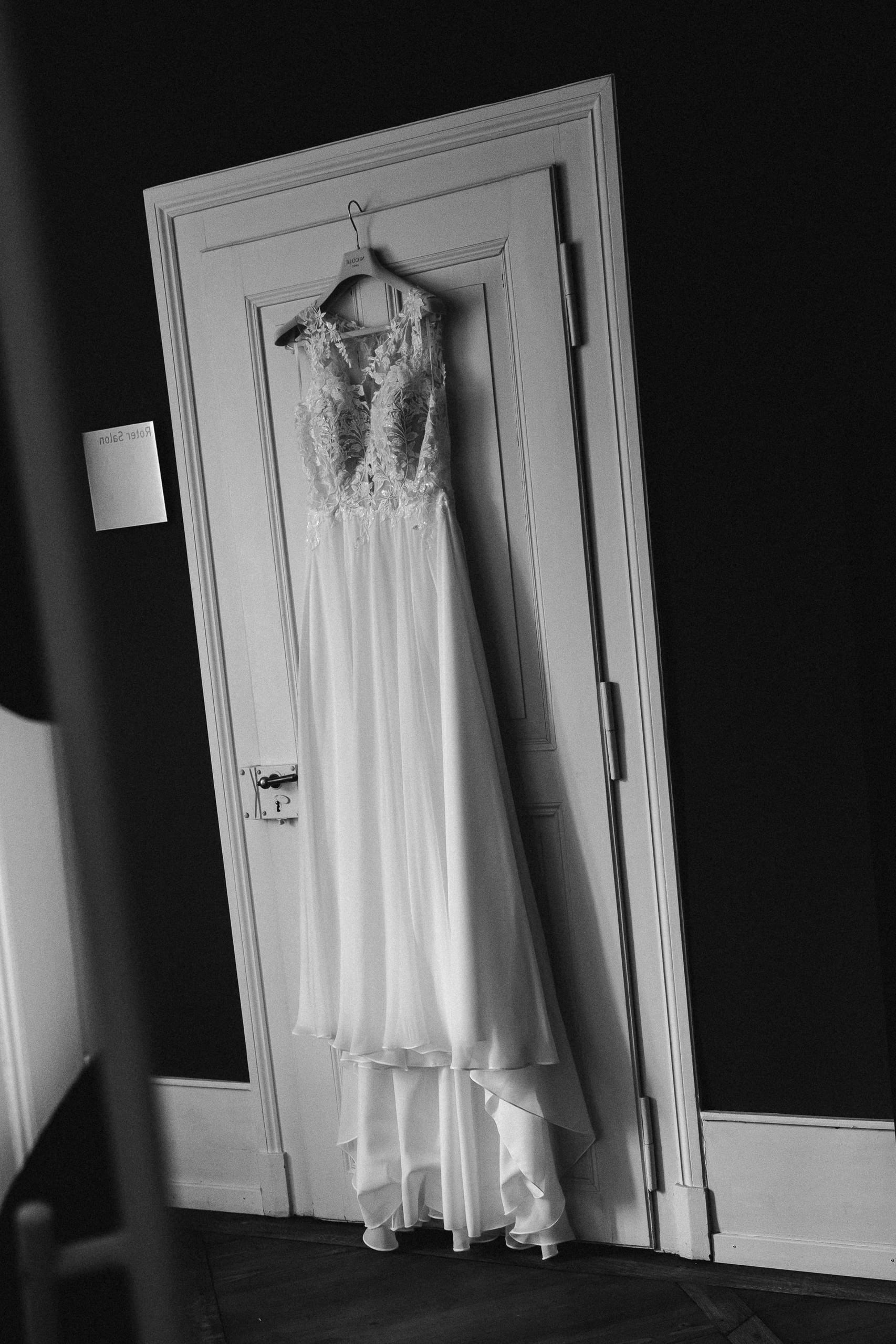 Schwarzweiss: Das Brautkleid hängt an einer Zimmertür