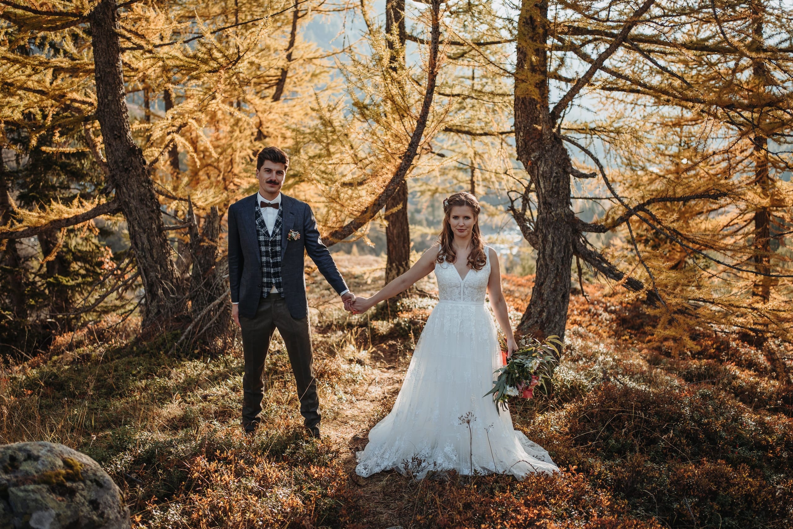 Das Brautpaar Hand in Hand im goldenen Lärchenwald