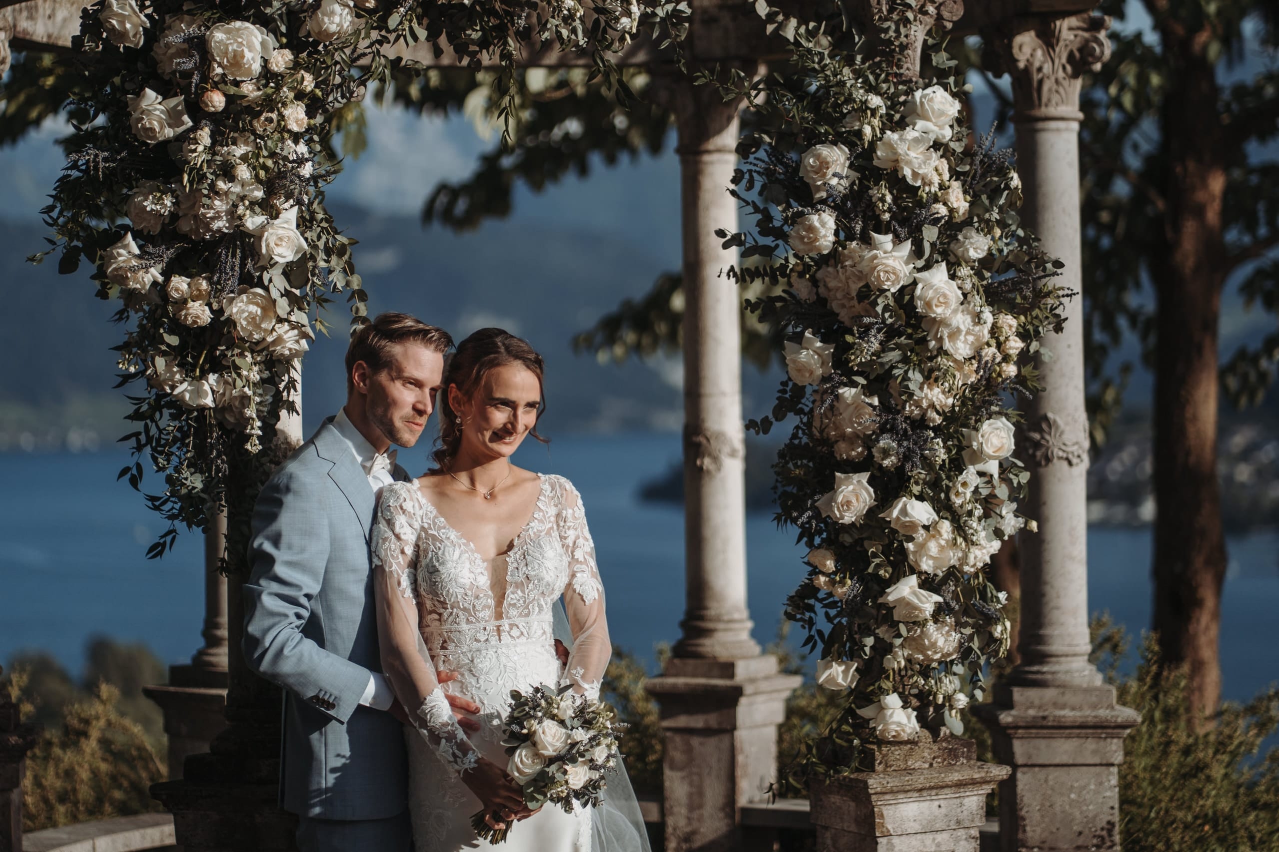 Das Brautpaar zwischen Säulen und Rosen, dahinter der See