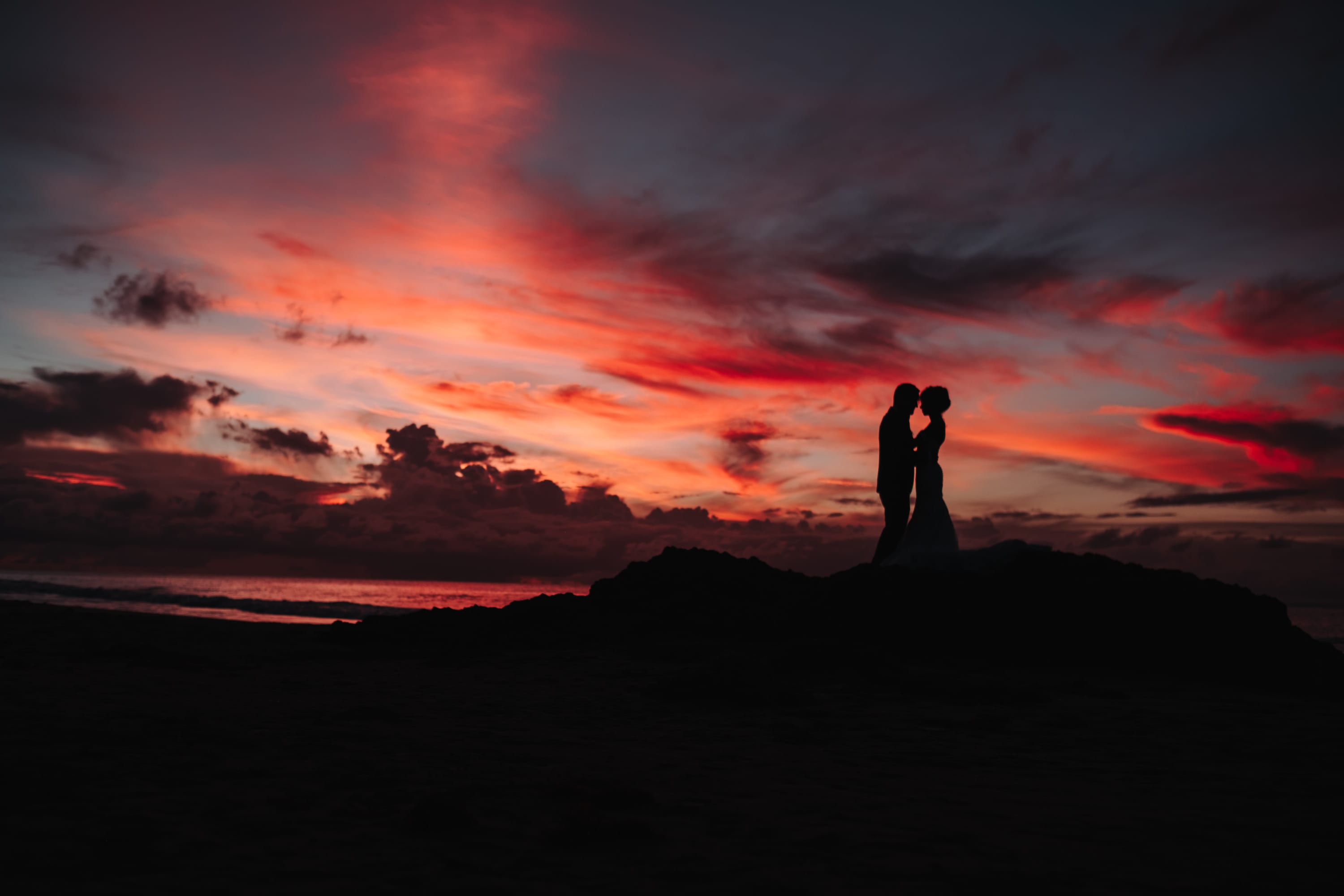 Das Brautpaar als Silhouette auf einem Felsen vor glühend rotem Abendhimmel