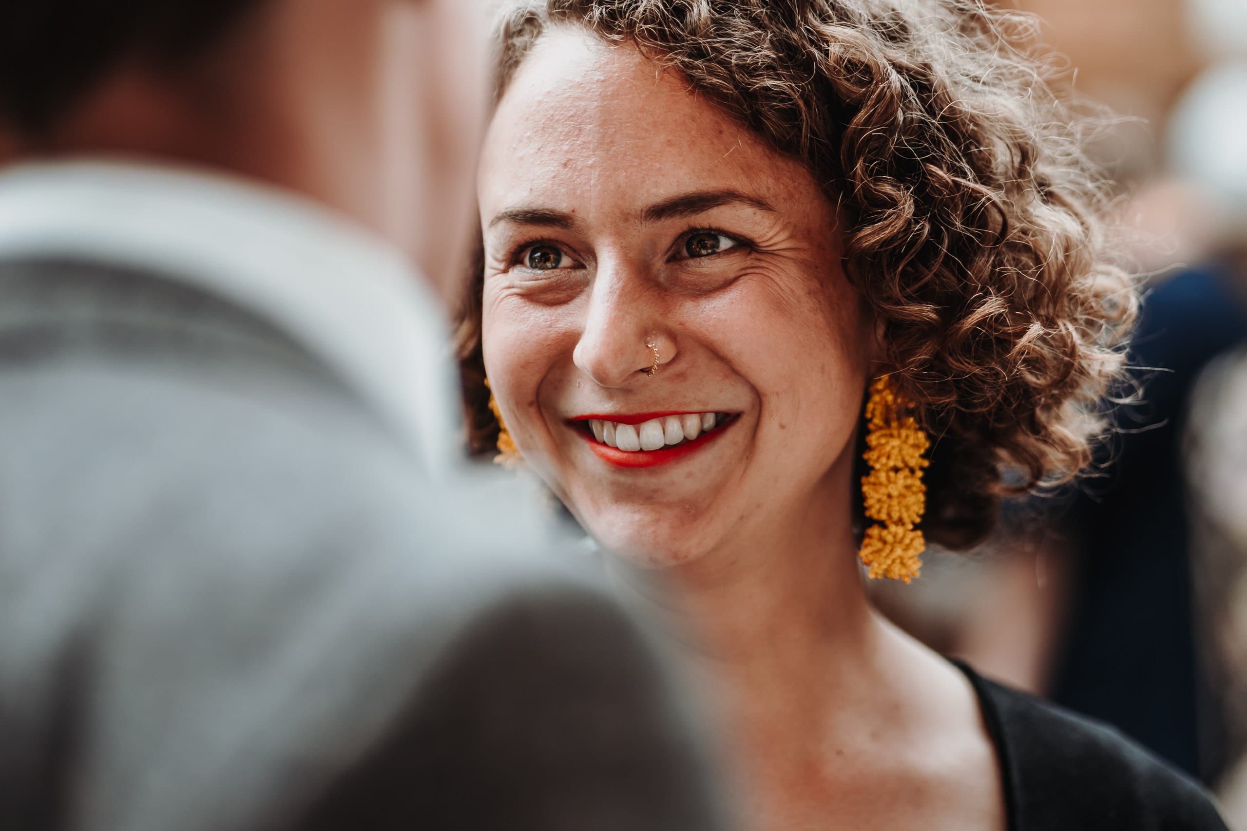 Eine Frau mit Locken und orangen Ohrringen lacht