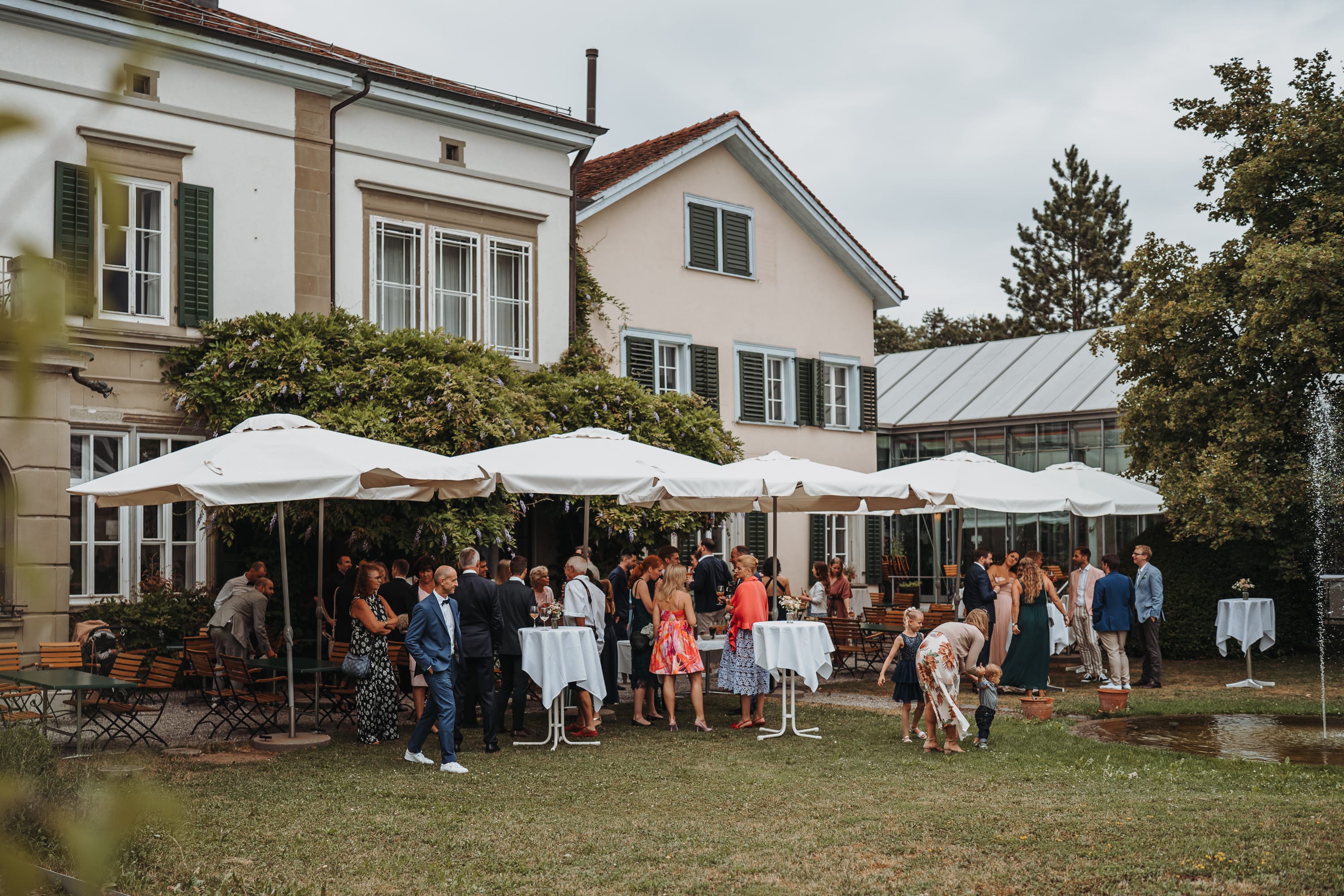 Gäste unter Sonnenschirmen im Garten vor dem Landhaus des Schöngrün