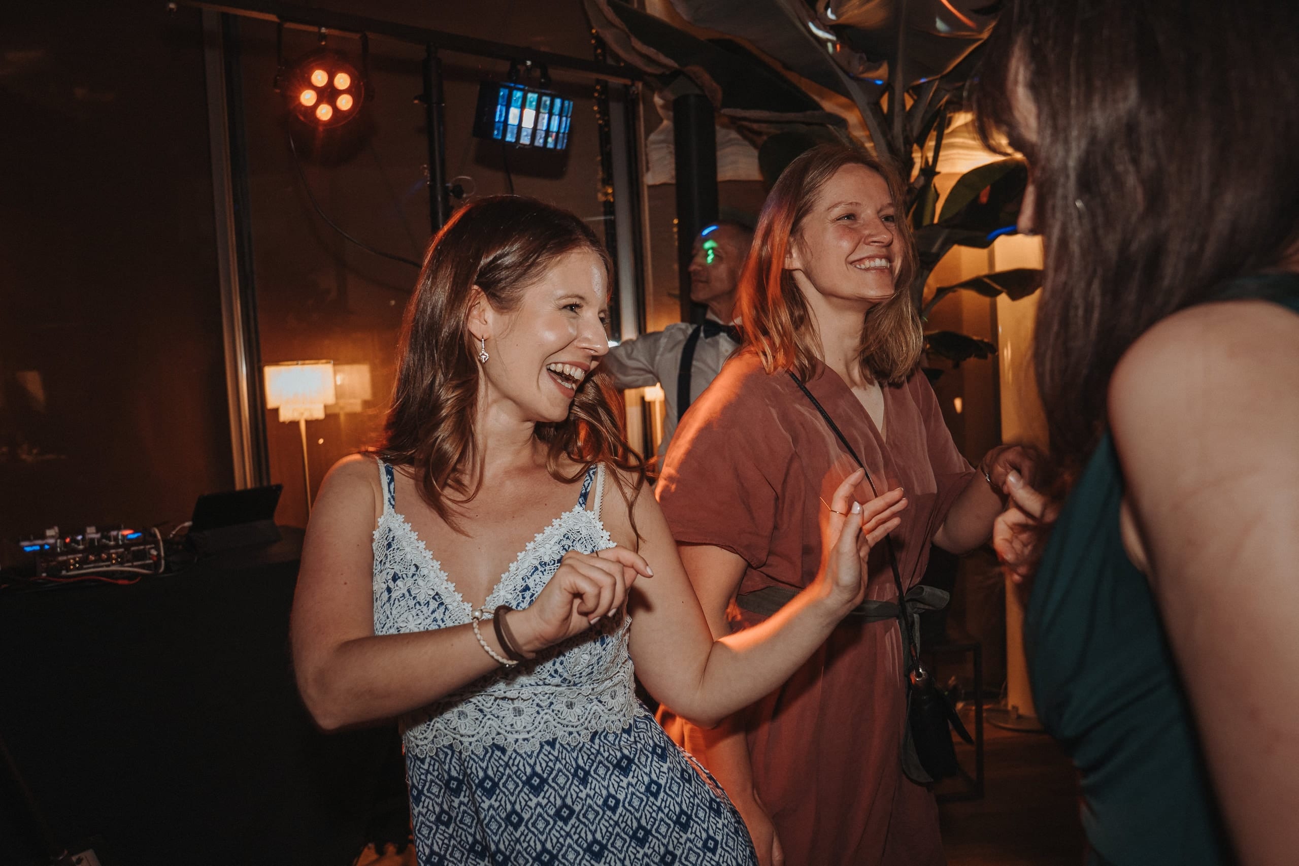 Zwei Frauen tanzen lachend neben dem DJ-Pult