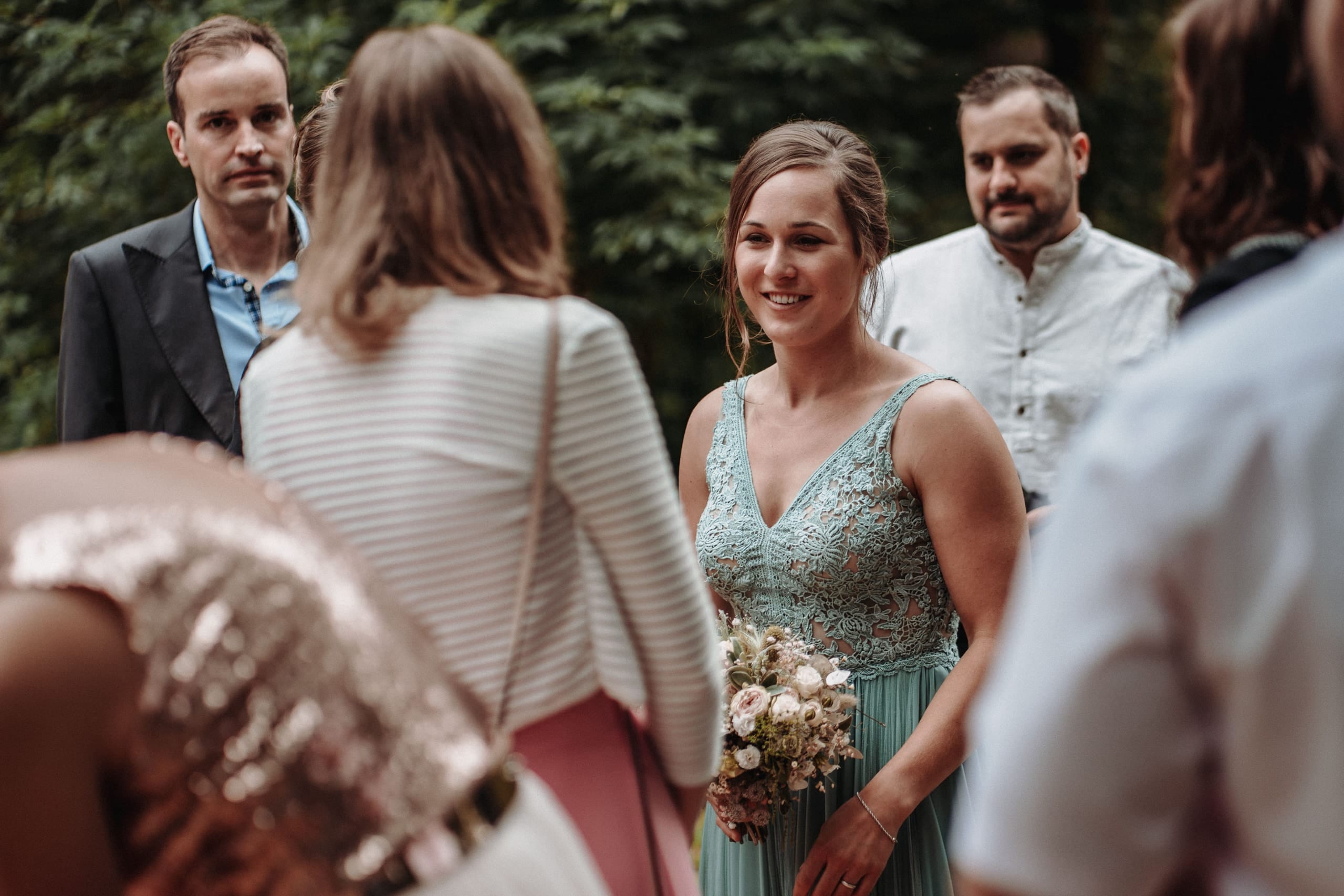Gäste warten auf die Trauung, eine Frau im mintgrünen Kleid hält einen Strauss