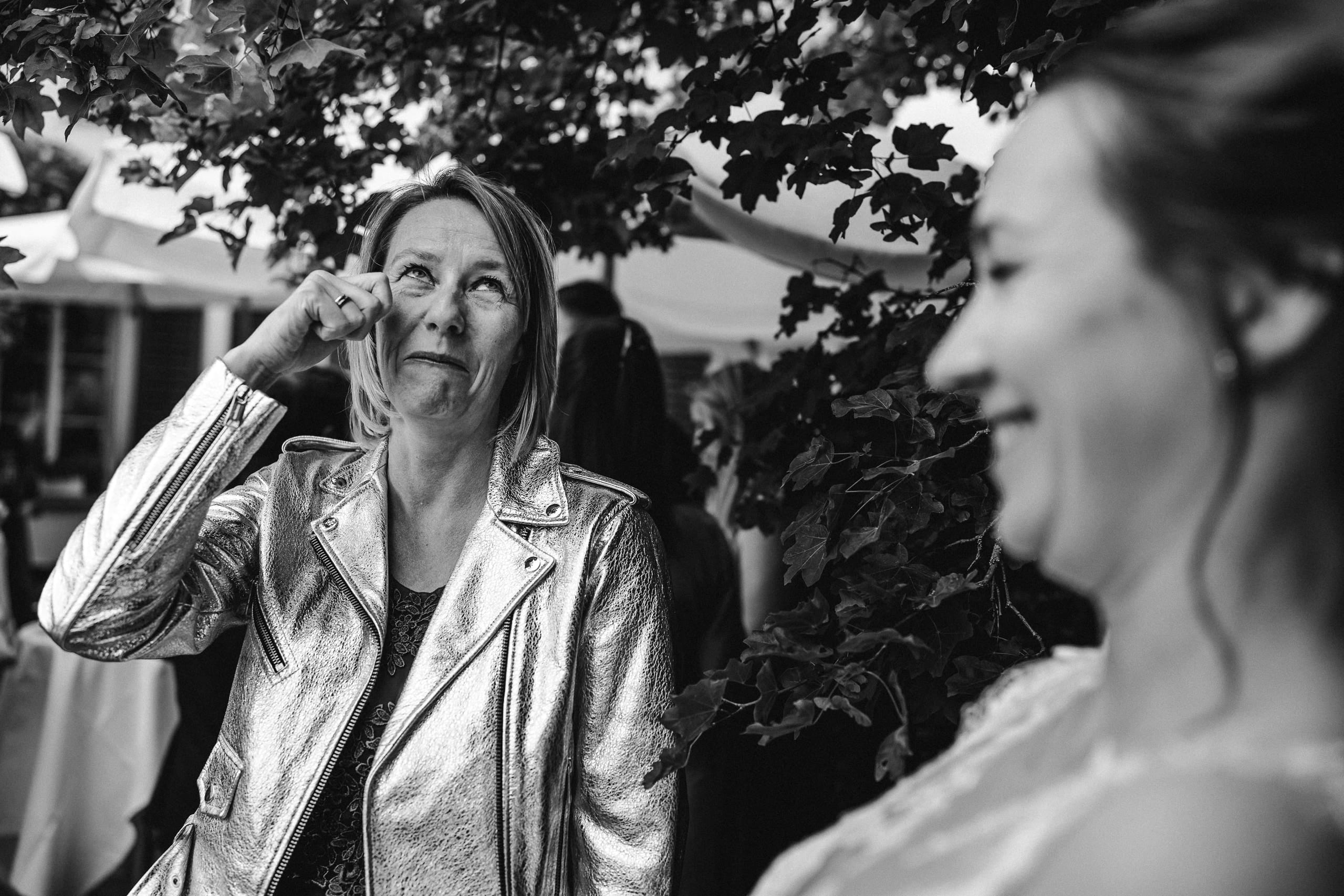 Schwarzweiss: Eine Frau in Silberjacke wischt sich eine Träne ab