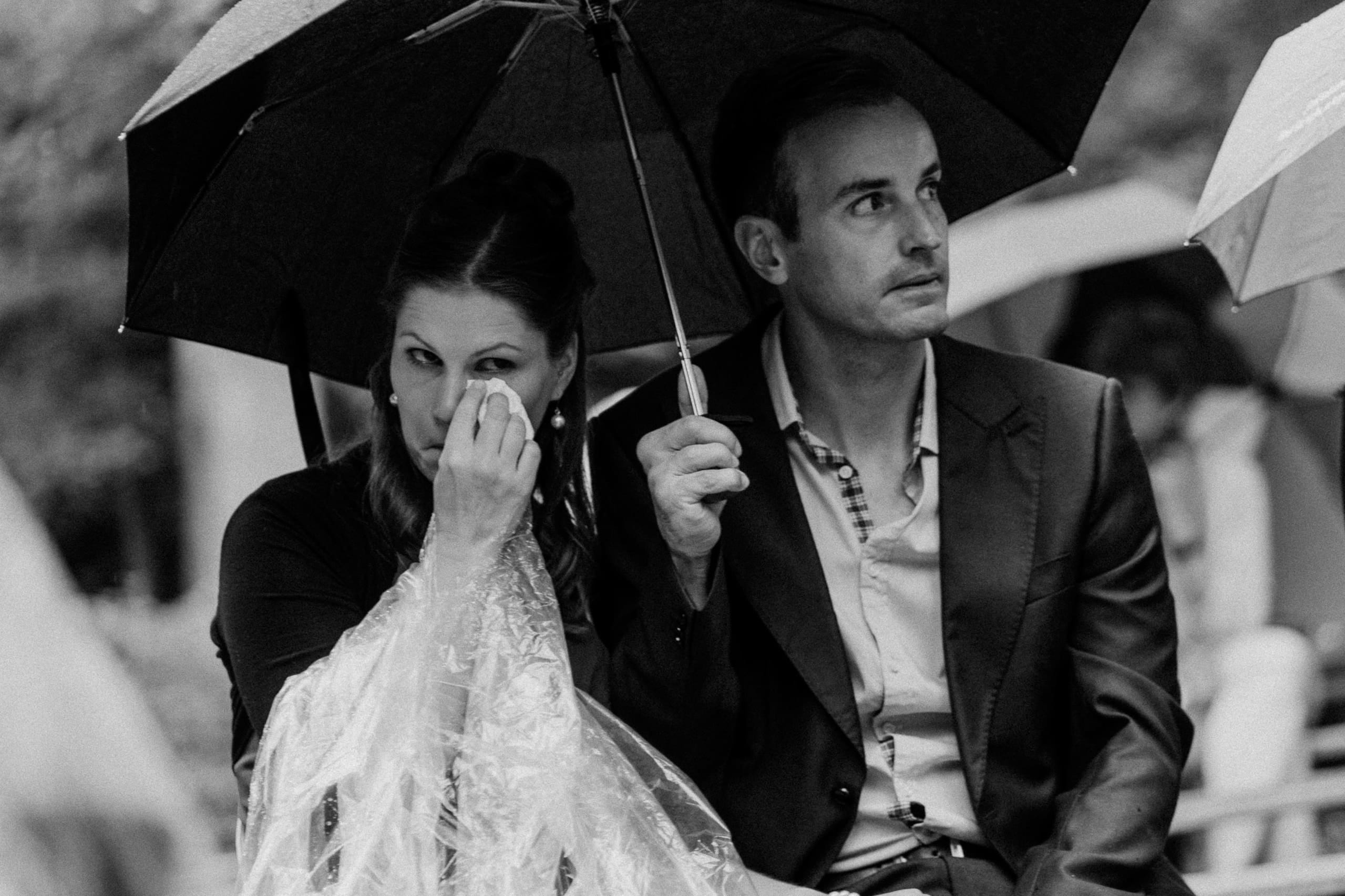 Schwarzweiss: Ein Gast wischt sich unter dem Regenschirm Tränen ab