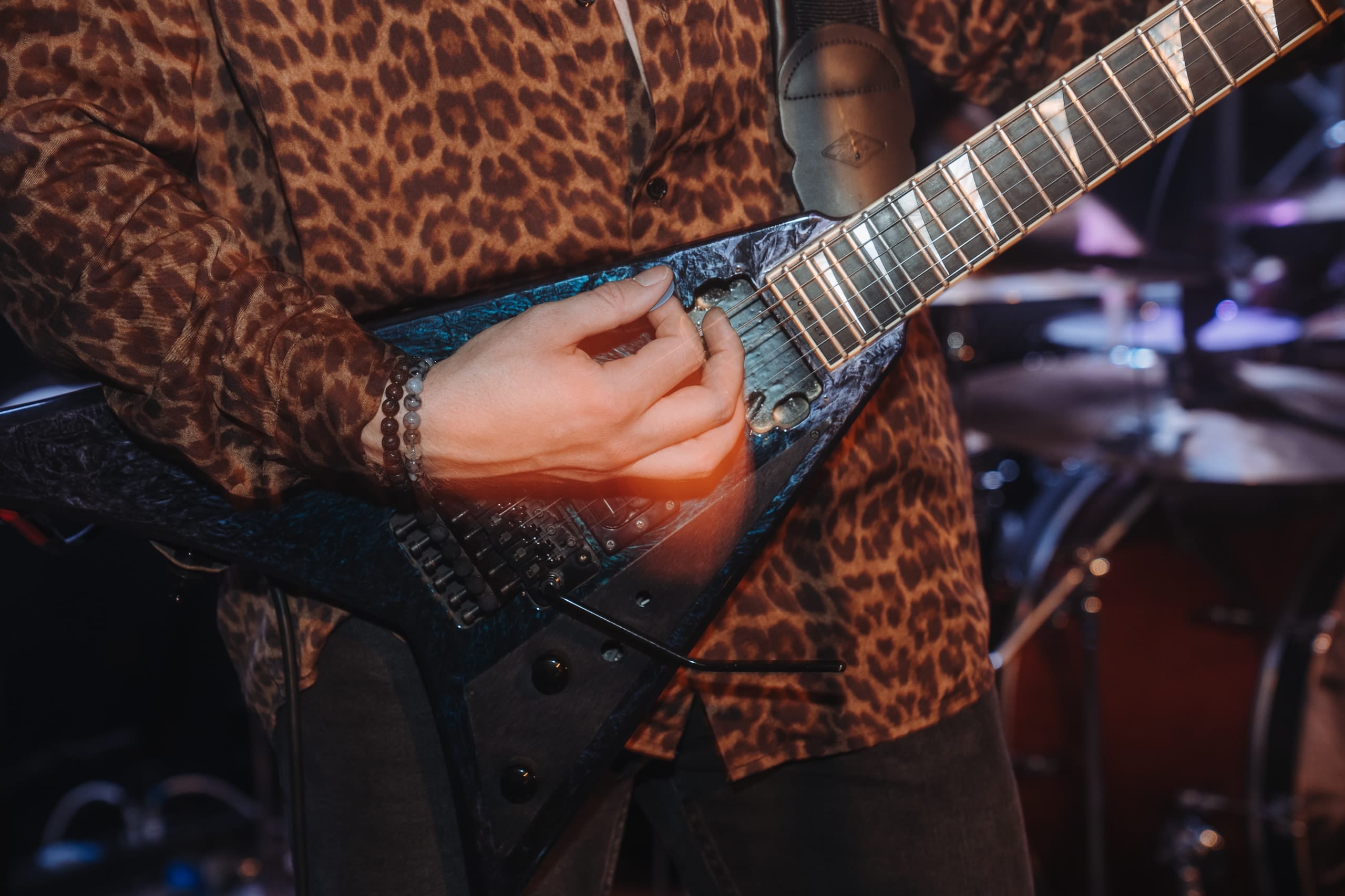 Nahaufnahme: eine Hand an einer Gitarre in Pfeilform, dahinter ein Leopardenhemd