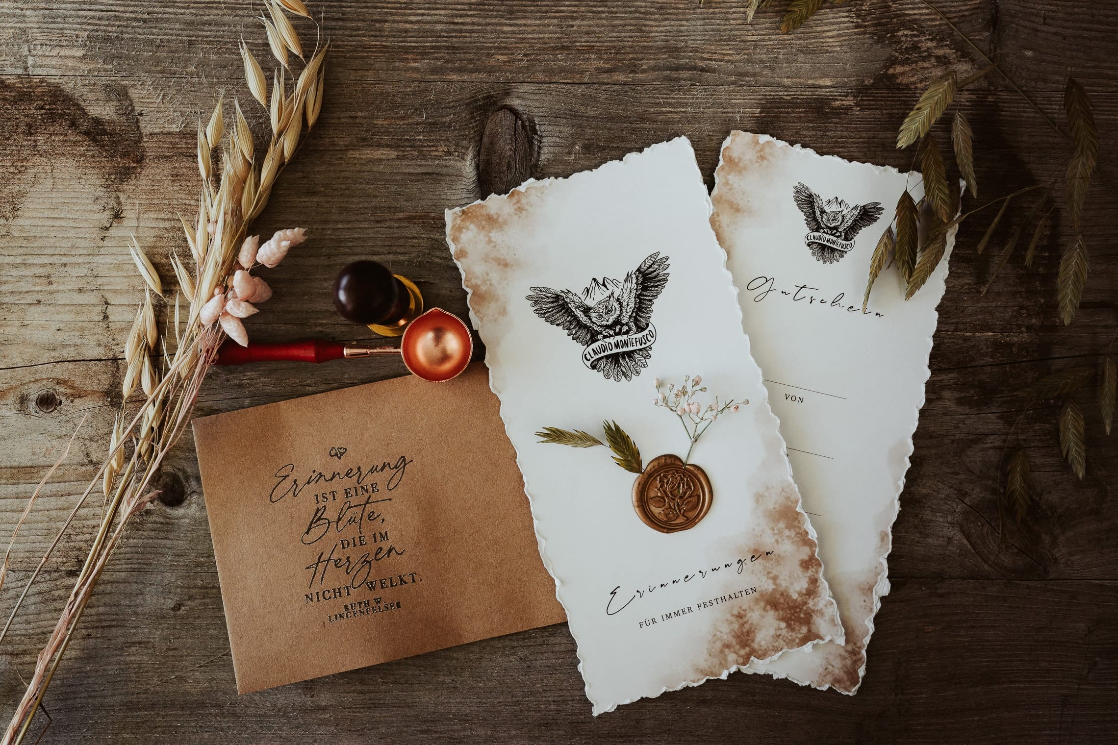 Zwei Gutscheinkarten mit gerissenem Rand, Eulen-Logo und kupferfarbenem Wachssiegel auf einem alten Holztisch, daneben ein Umschlag aus Kraftpapier, ein Siegelstempel, ein Wachslöffel und Trockengräser
