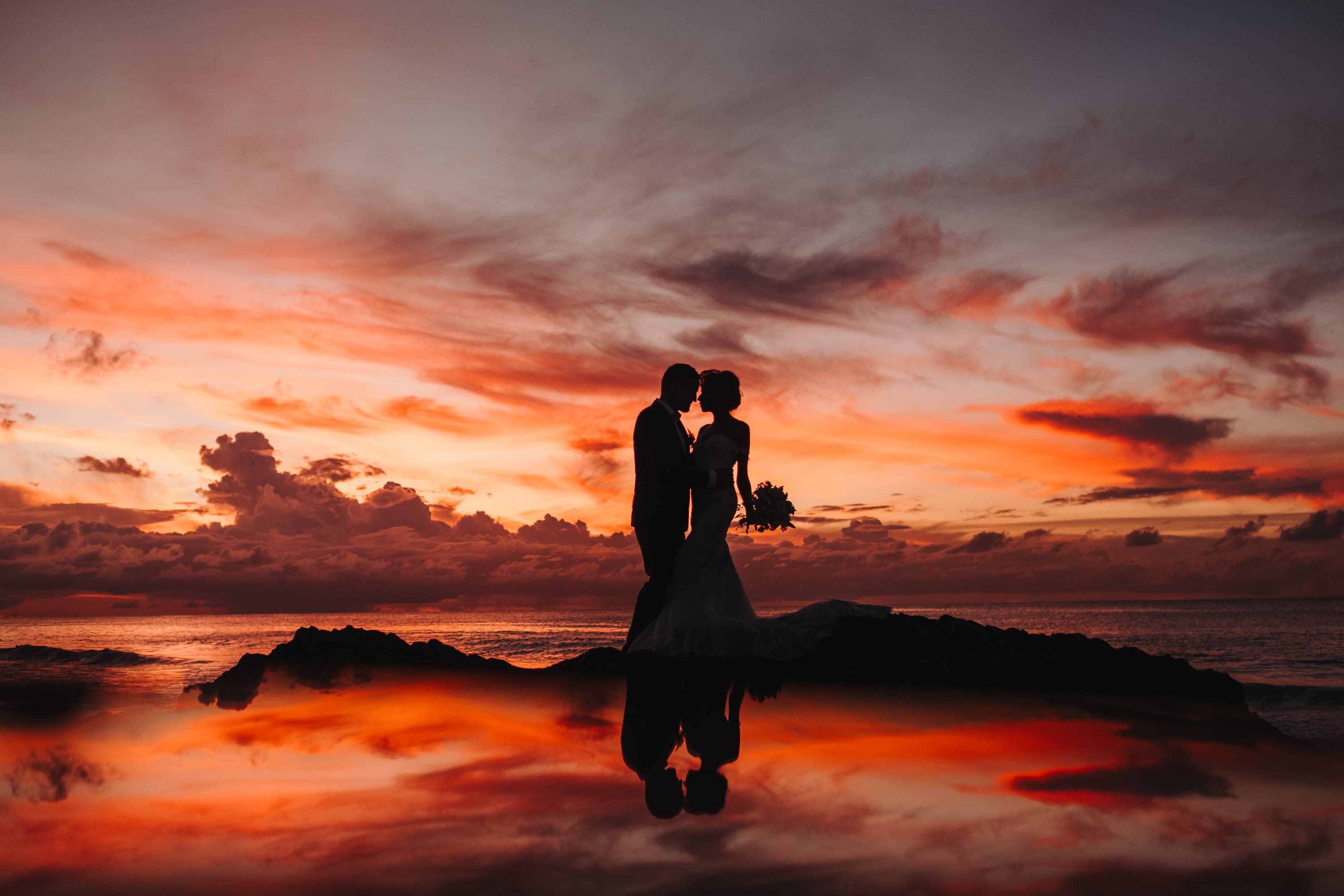 Sonnenuntergang auf Tobago: das Brautpaar als Silhouette auf einem Felsen, Himmel und Paar spiegeln sich im Wasser