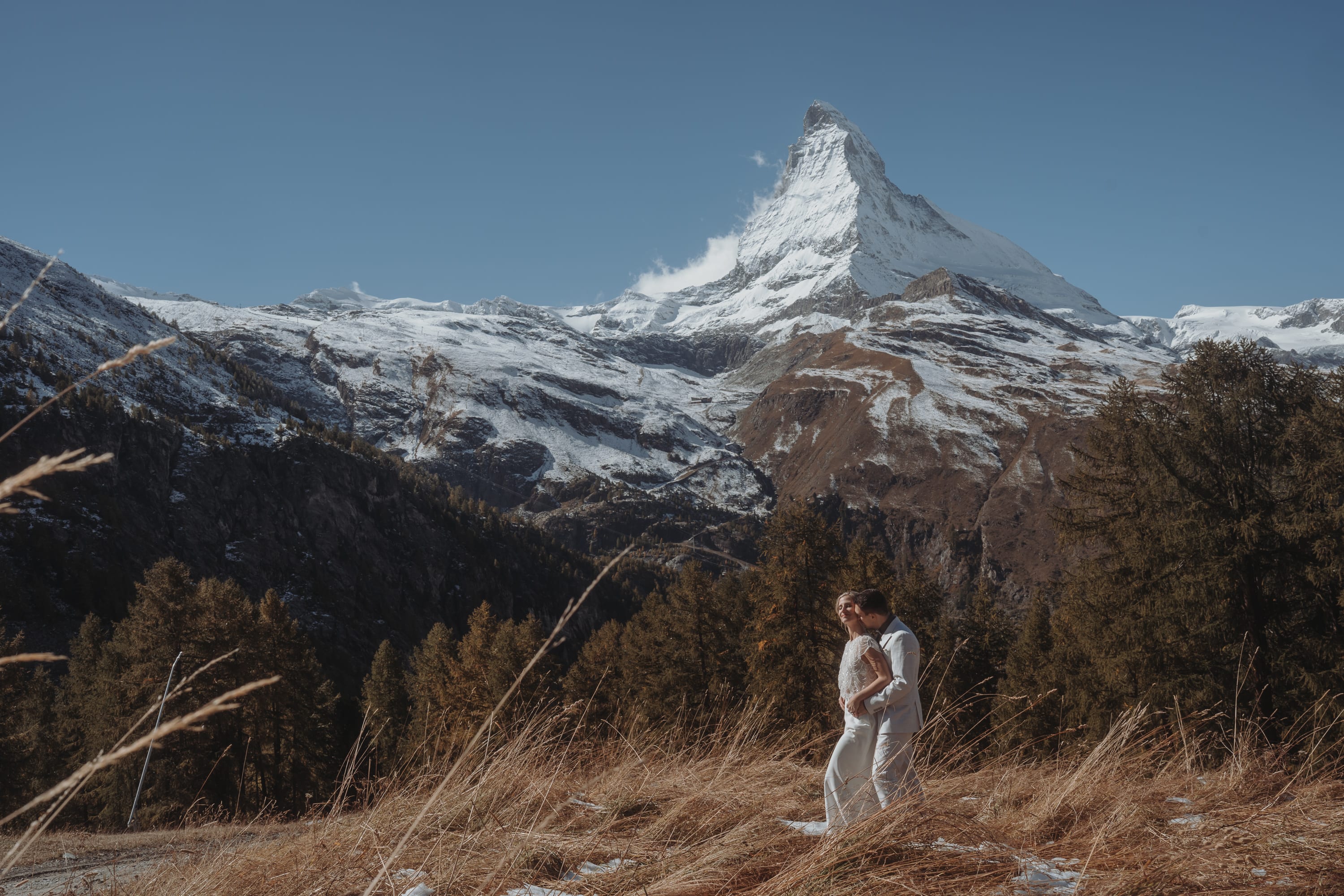 Das Brautpaar umarmt sich in der Herbstwiese oberhalb von Zermatt, dahinter das Matterhorn