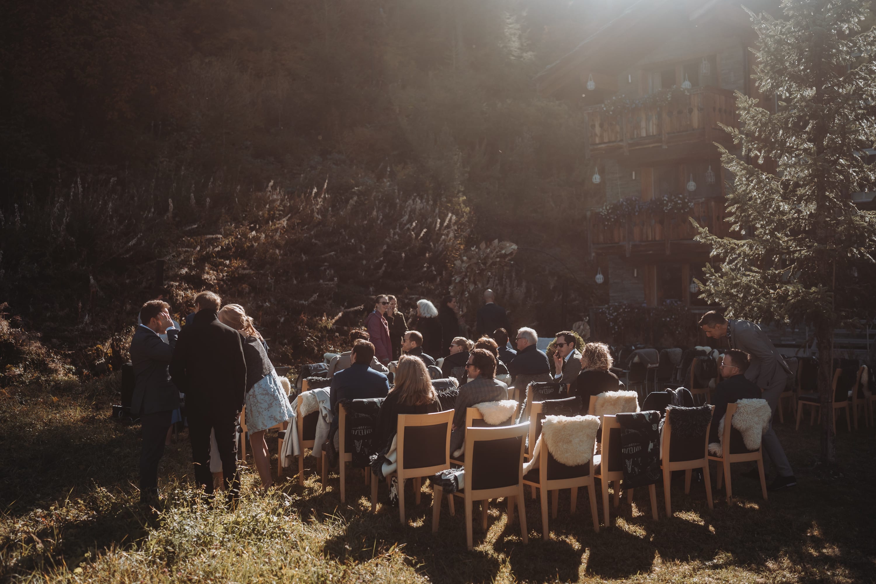 Die Hochzeitsgäste nehmen im Gegenlicht im Garten Platz
