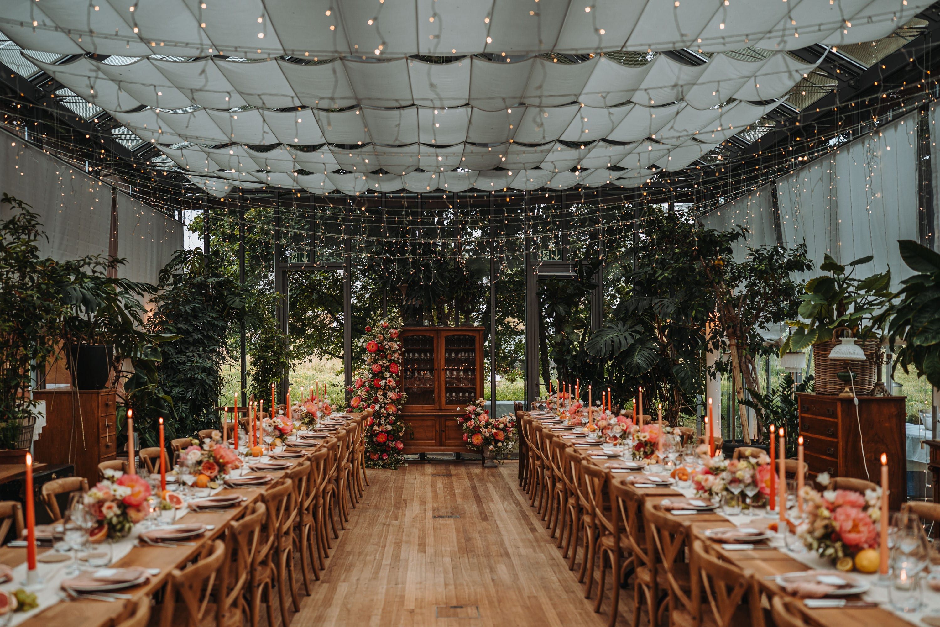 Der dekorierte Hochzeitssaal im Glashaus des Schöngrün mit langen Tafeln unter Lichterketten