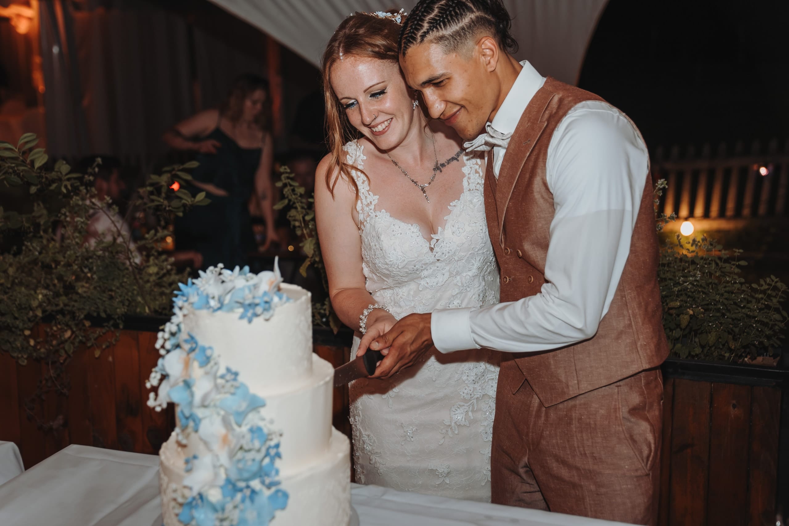 Das Brautpaar schneidet die Hochzeitstorte mit blauen Blüten an