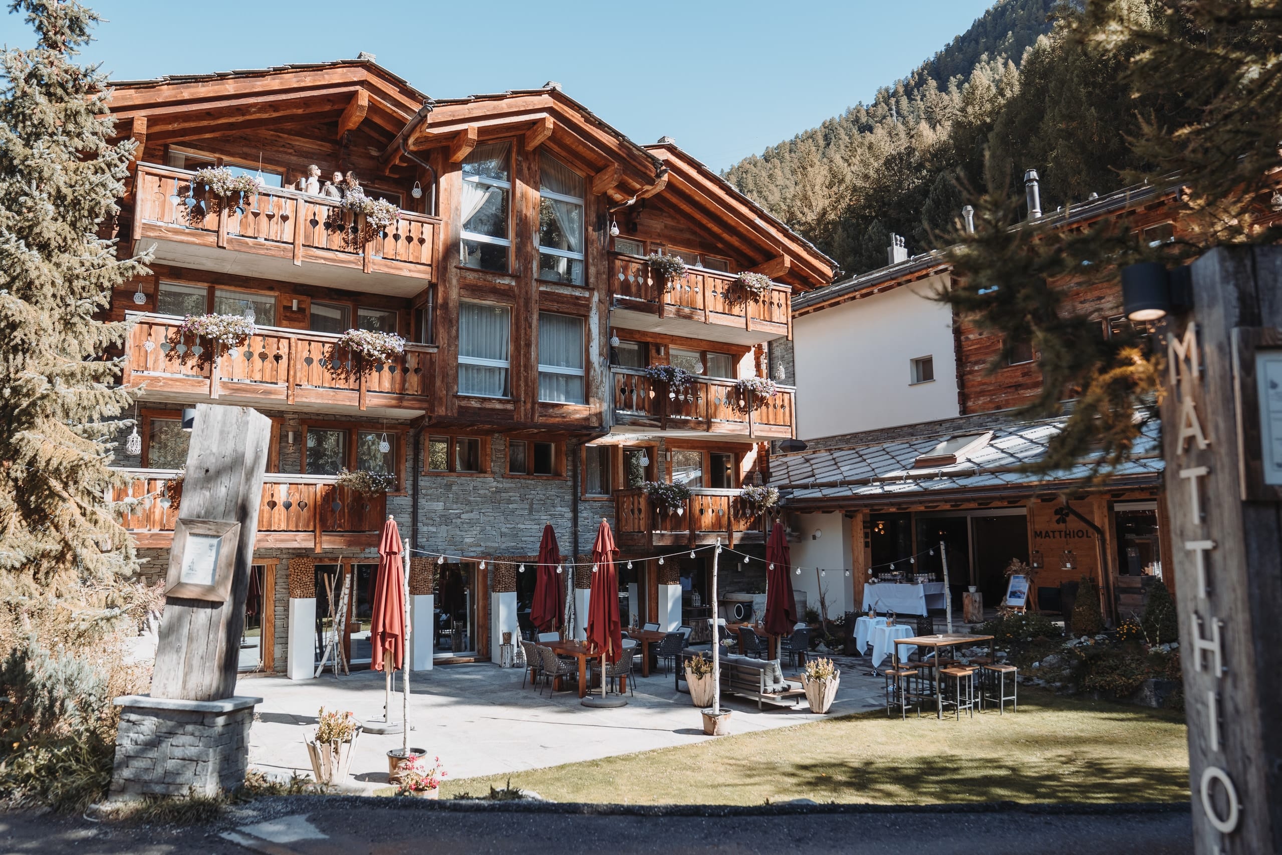 Die Terrasse des Hotels Matthiol mit Holzbalkonen und roten Sonnenschirmen