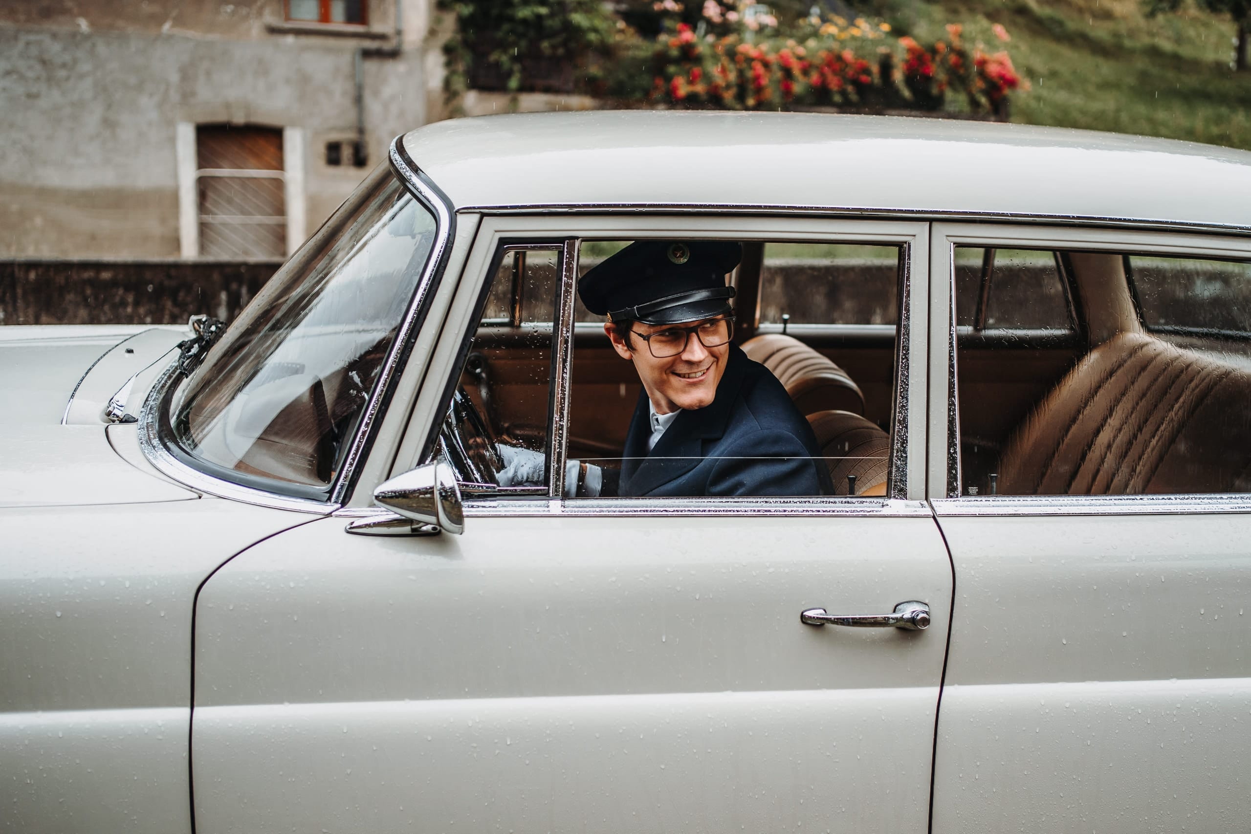 Ein Kollege mit Chauffeurmütze am Steuer des alten Mercedes