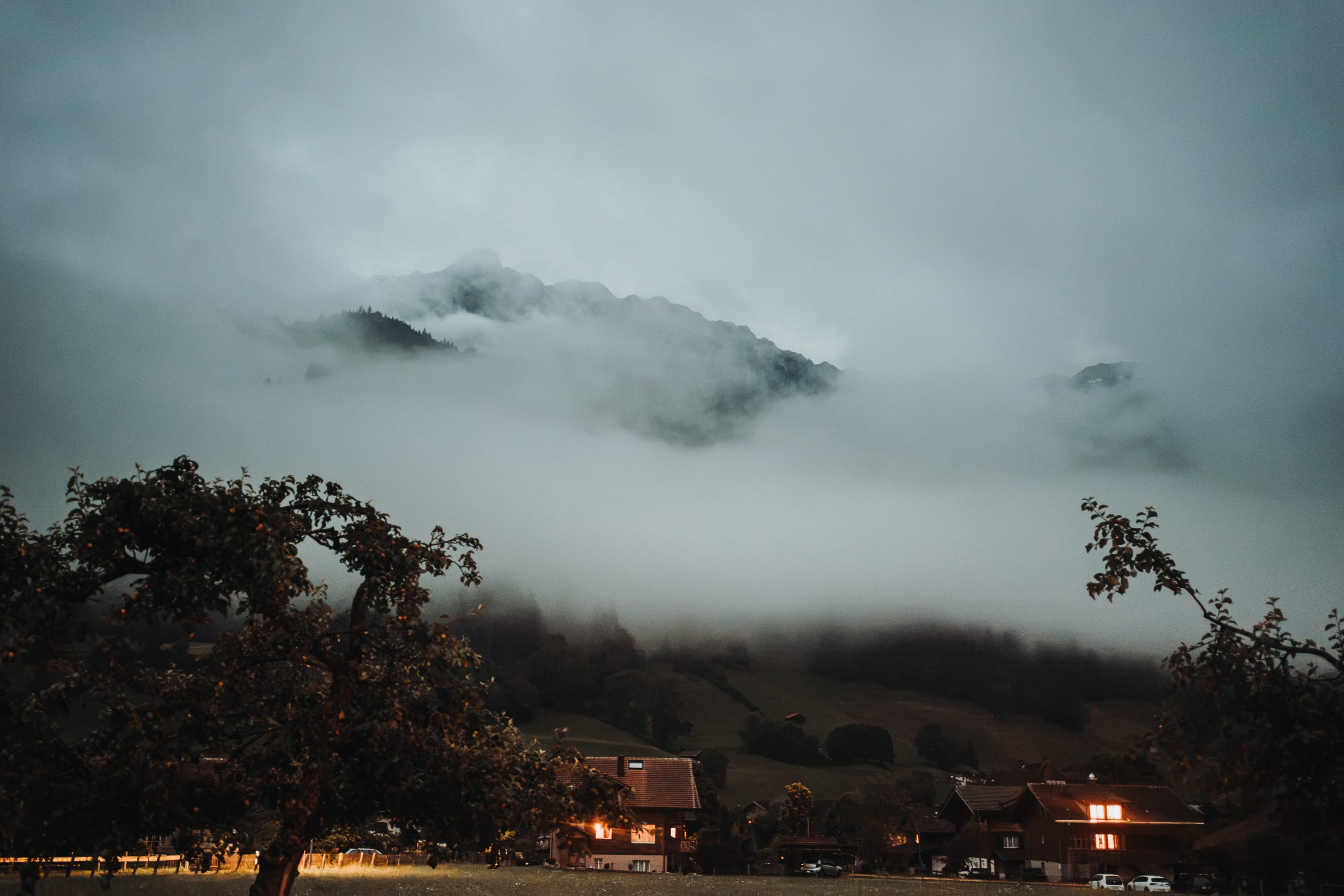 Nebel über den Bergen in der Dämmerung, darunter beleuchtete Häuser