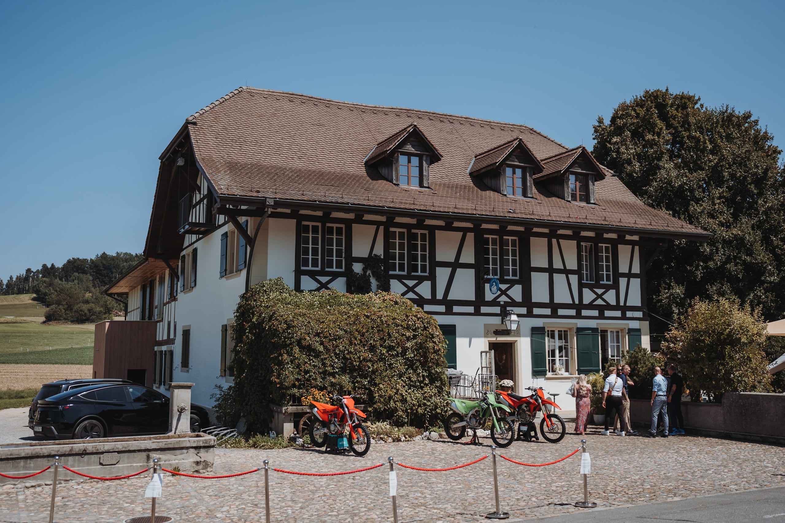 Ein Riegelhaus unter blauem Himmel, davor Motorräder und eine rote Absperrkordel