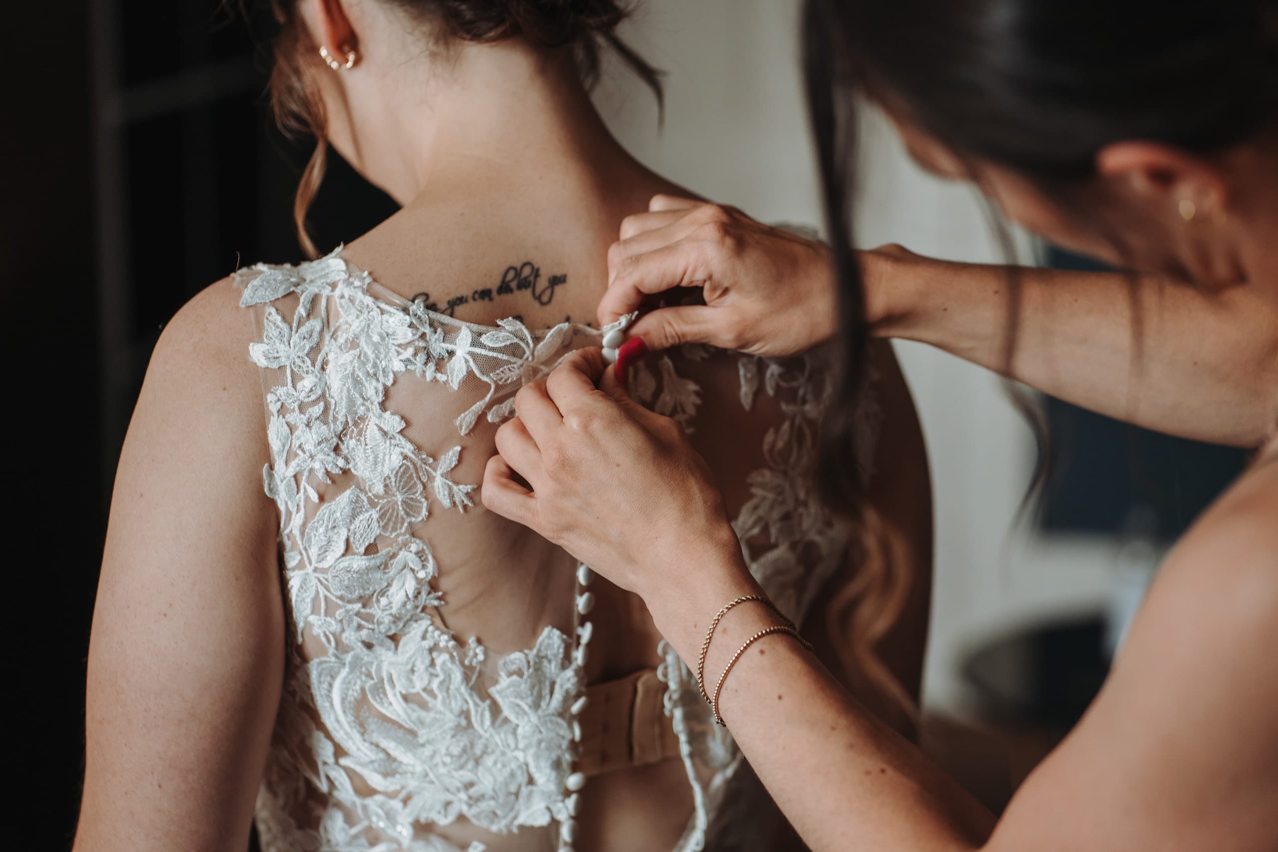 Eine Frau knöpft der Braut das Spitzenkleid zu, ganz nah
