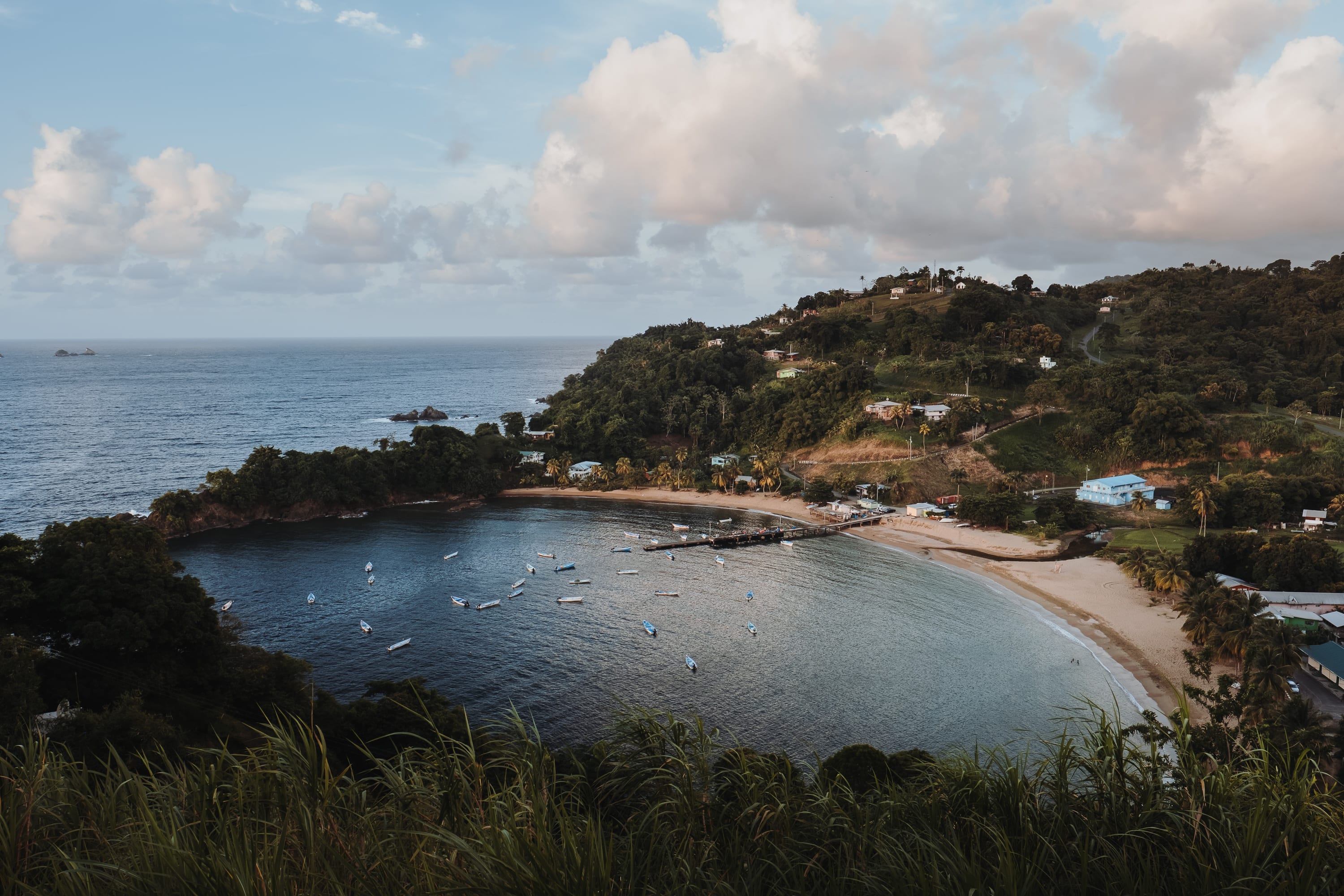 Blick von oben auf eine Bucht auf Tobago mit kleinen Booten, einem Steg und grünen Hügeln