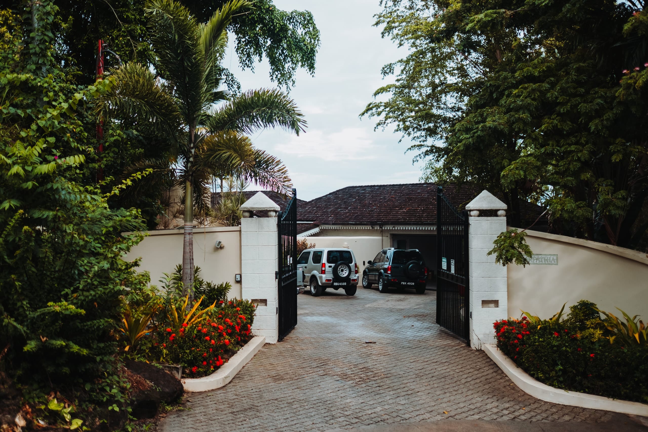 Offenes Tor zur Villa Carpathia, gesäumt von Palmen und roten Blumen