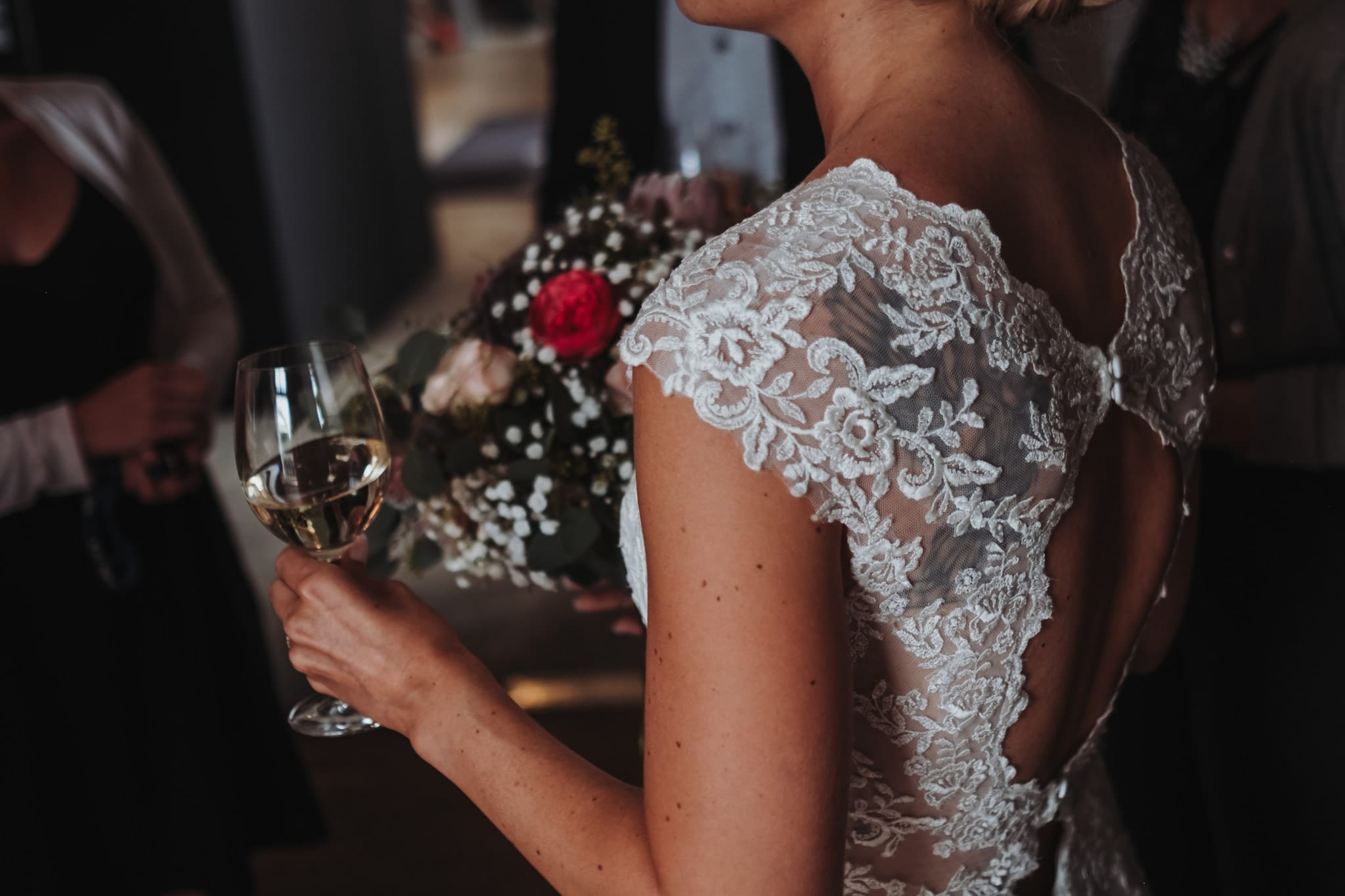 Nahaufnahme: das Spitzenkleid der Braut, ein Weinglas und eine rote Blume