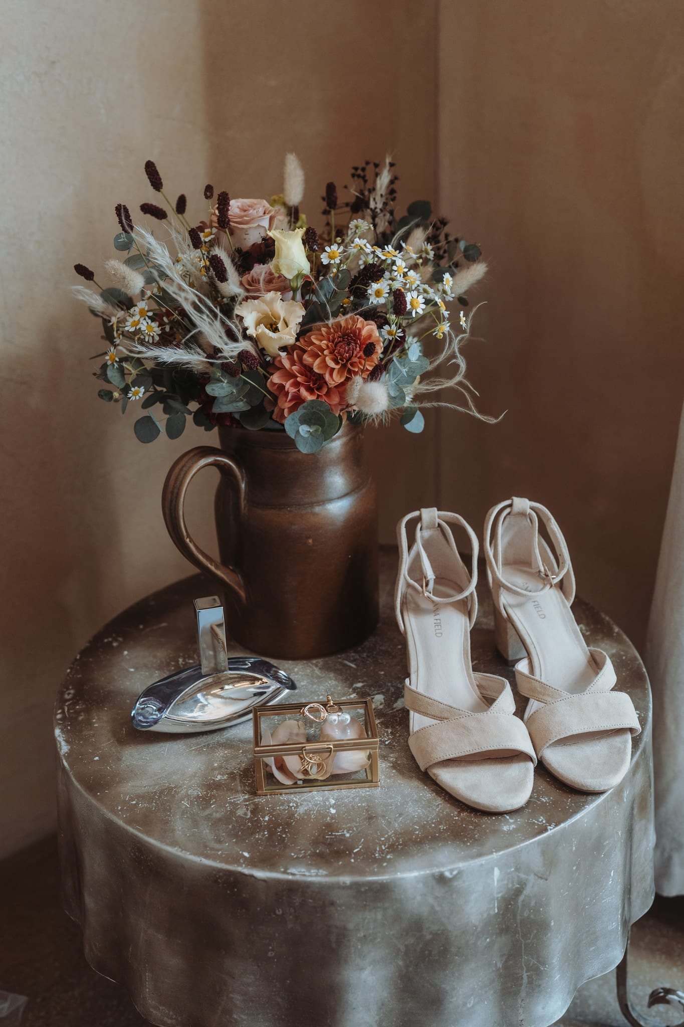 Brautschuhe, ein kleines Glaskästchen und ein Krug mit Trockenblumen auf einem Tischchen, am Morgen der Hochzeit am Hasliberg