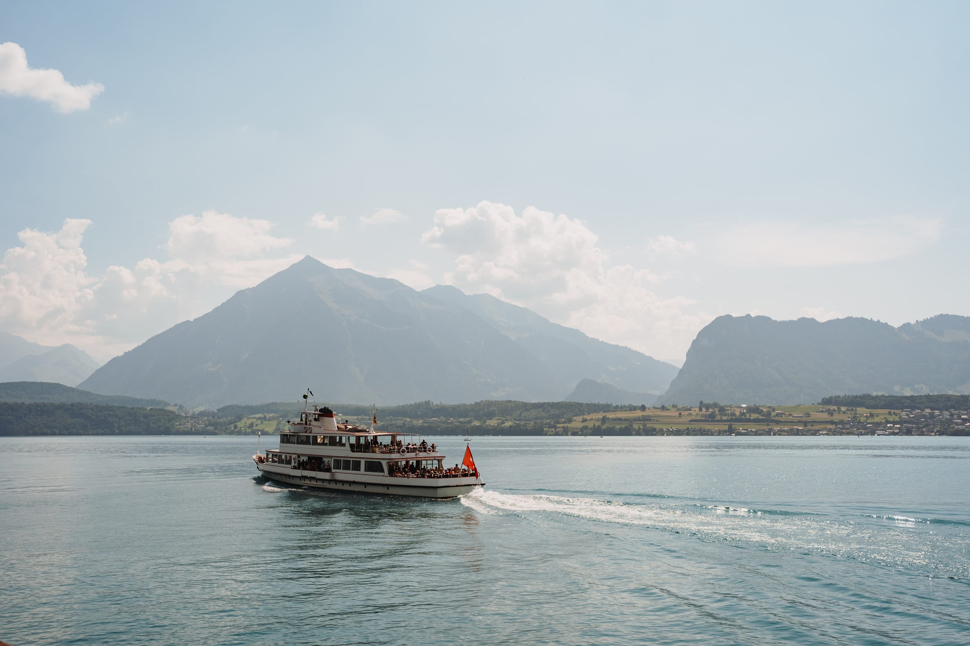 Ein Kursschiff fährt über einen See, dahinter ein spitzer Berg und weitere Gipfel