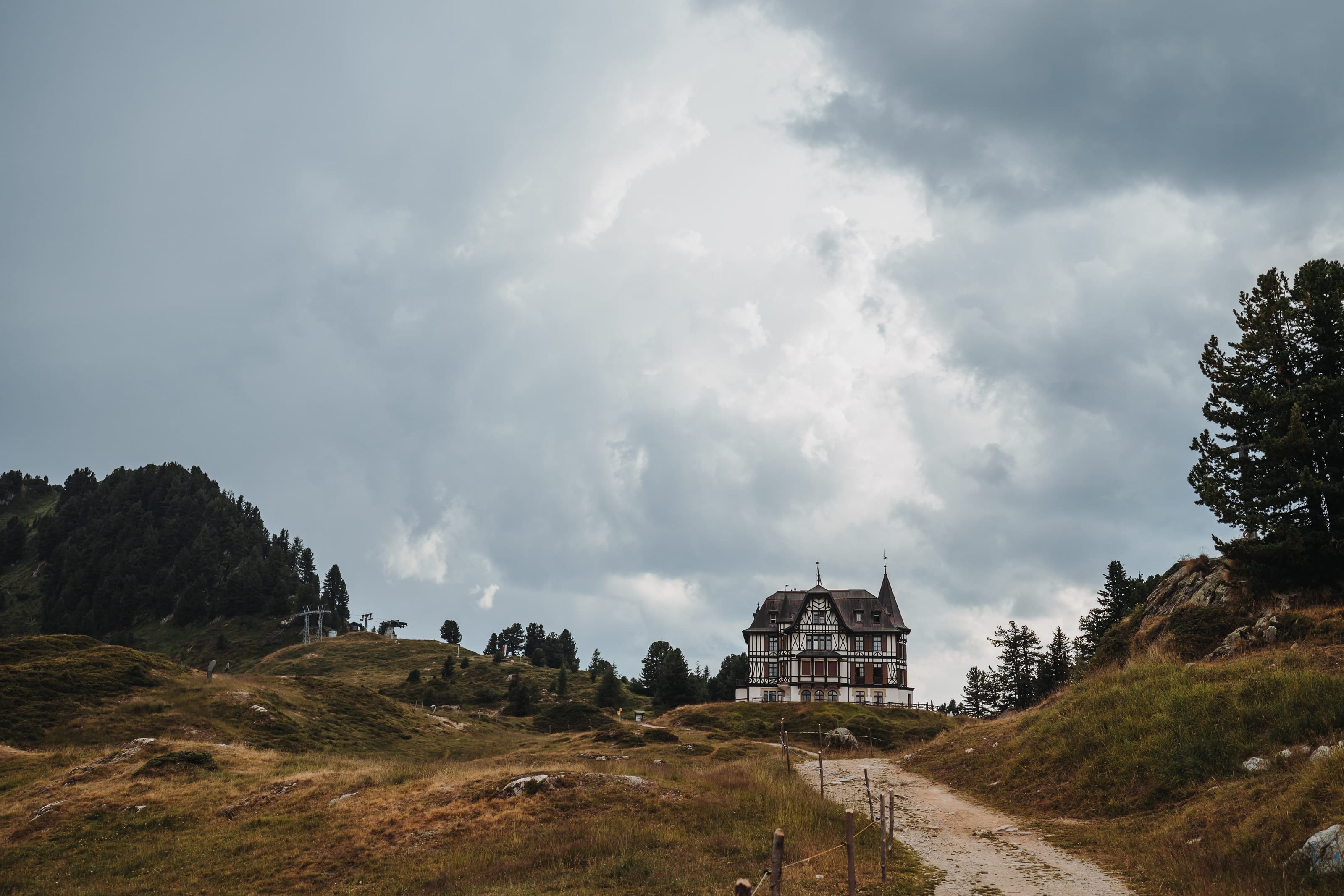 Ein Weg führt über die Alp bei der Riederalp zu einem alten Haus, darüber schwere Wolken