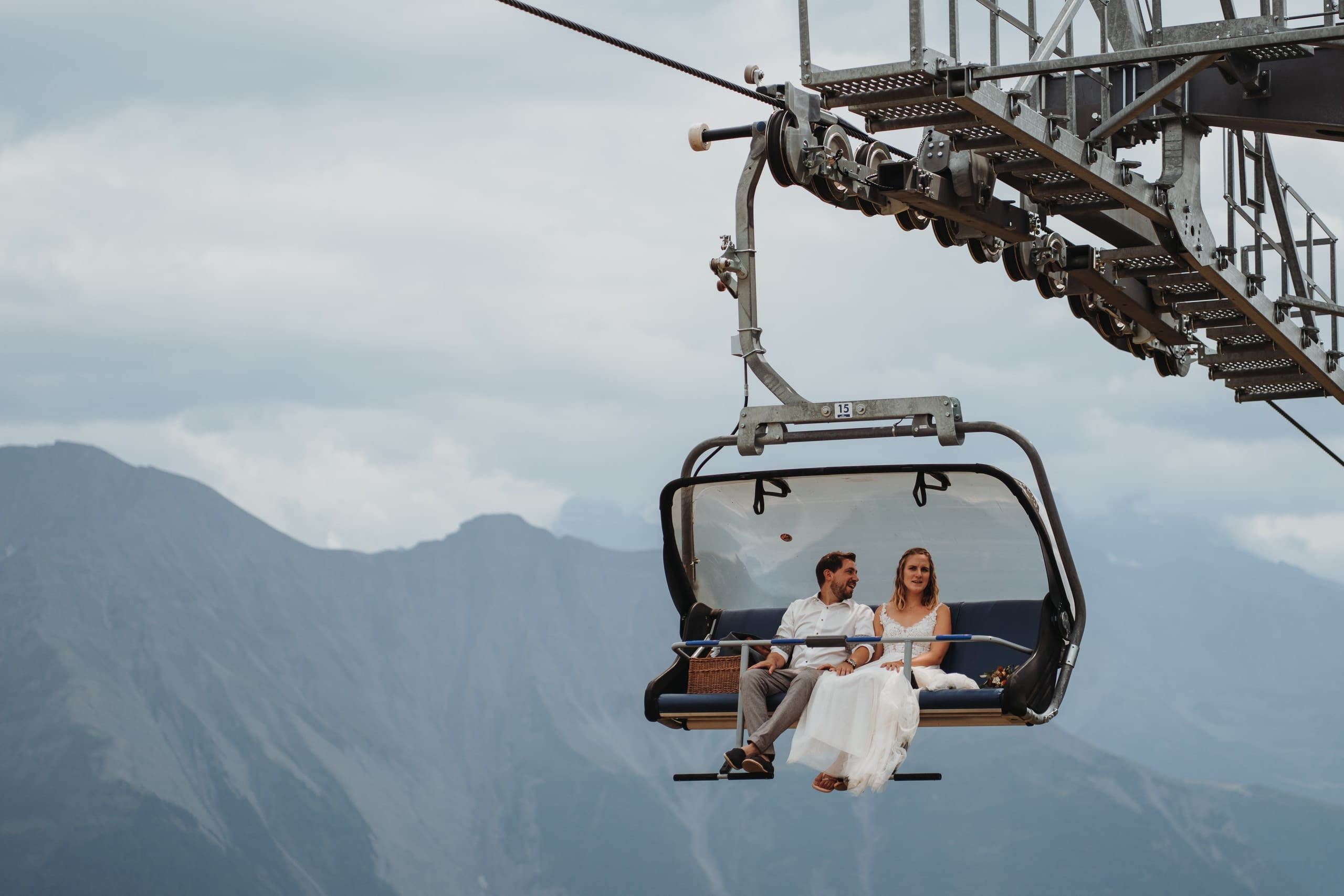 Das Brautpaar fährt lächelnd im Sessellift auf der Riederalp, dahinter die Berge
