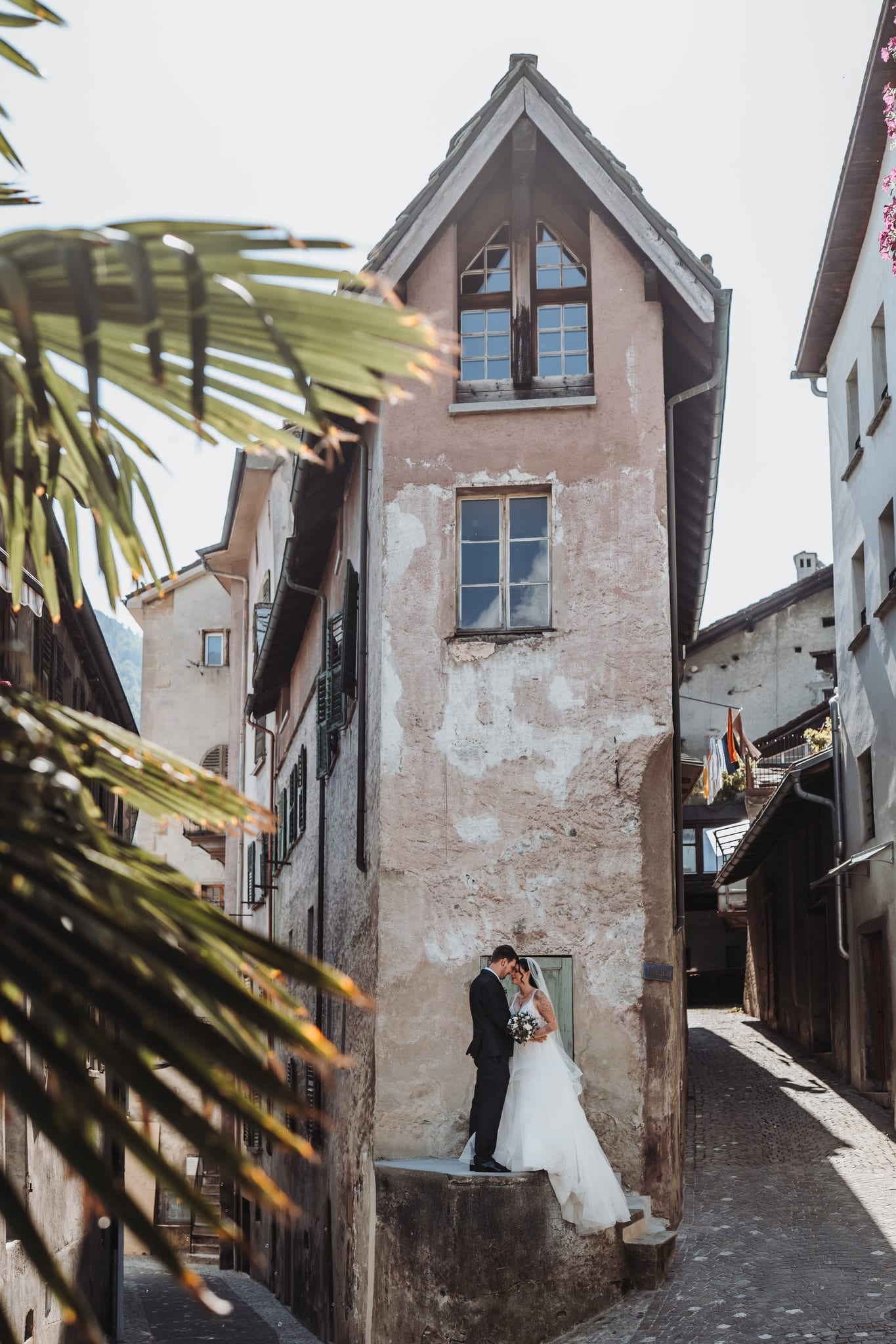 Das Brautpaar küsst sich vor einem alten, schmalen Haus in einer Gasse der Altstadt von Visp