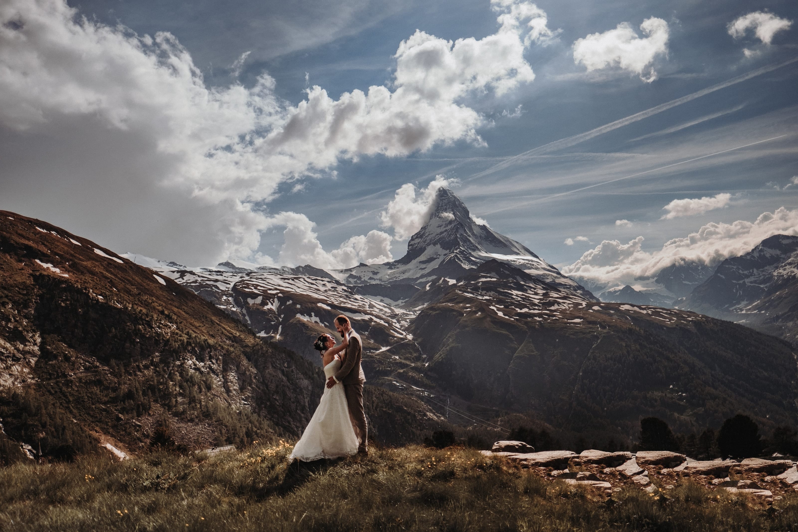 Das Brautpaar umarmt sich auf einer Bergwiese bei Zermatt, dahinter das Matterhorn unter einem weiten Wolkenhimmel
